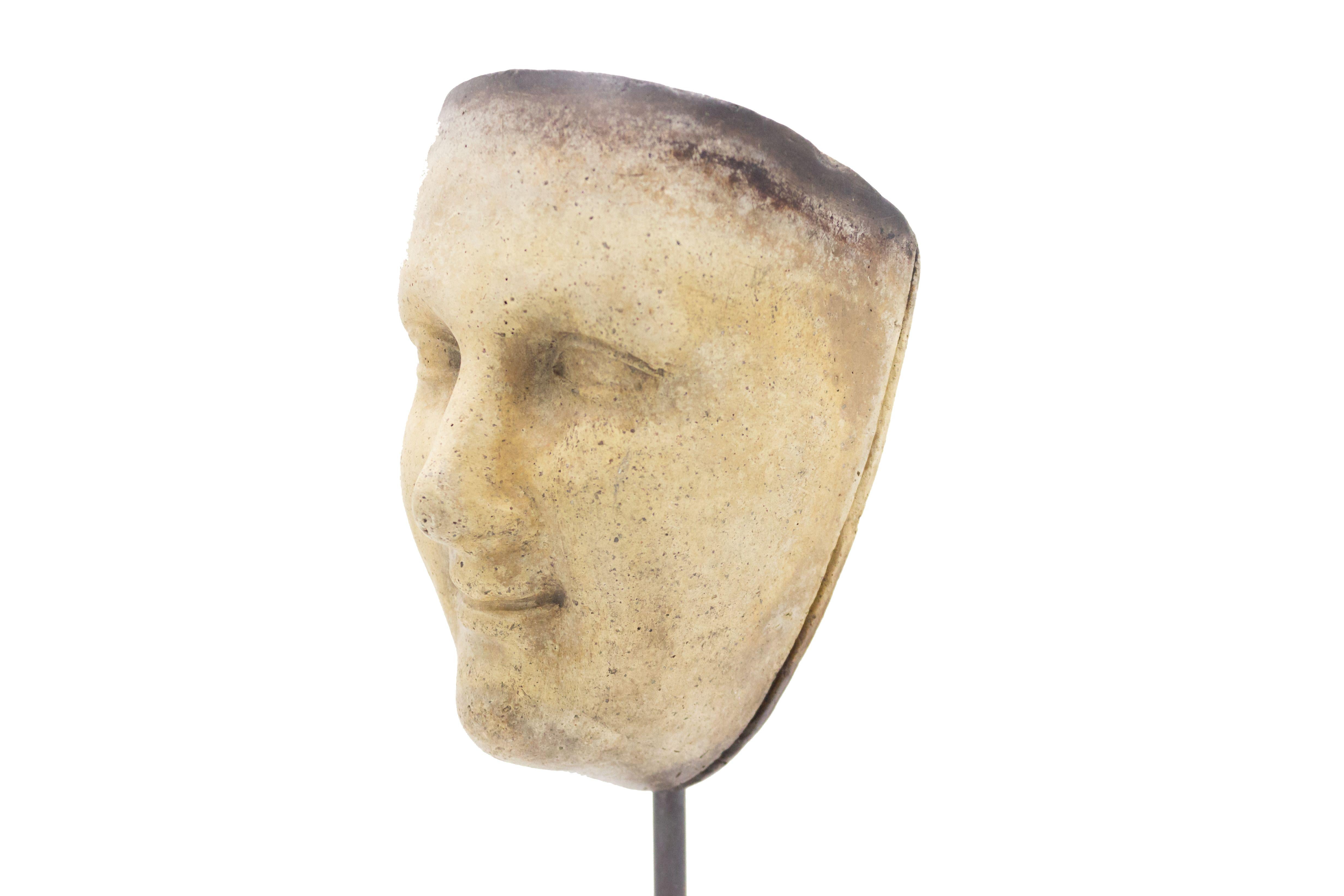 Continental German (late 19th Cent) sculpted terra-cotta master mask mold of a serene smiling face displayed on a square black marble base stand (part of a collection).
 