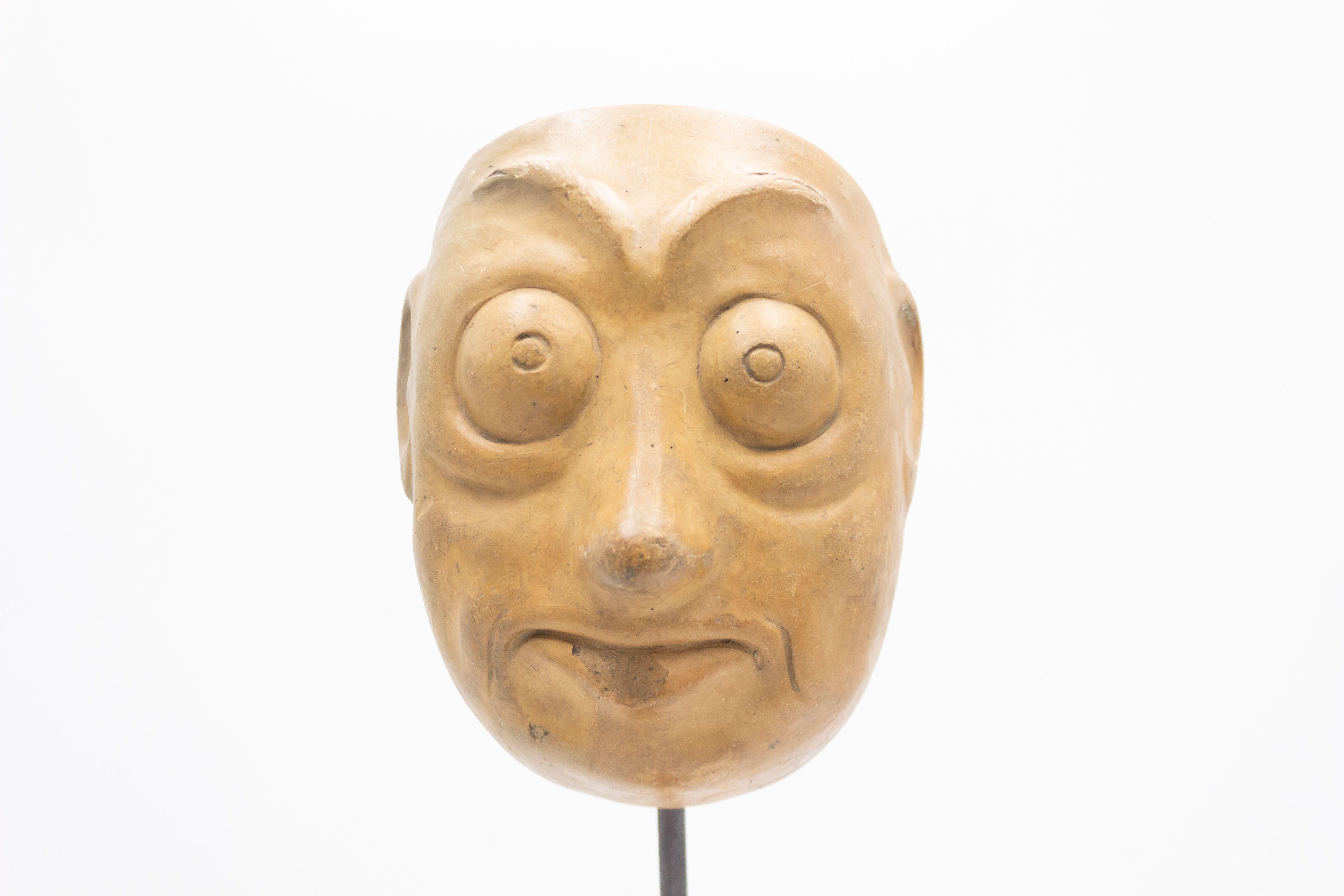 Continental German (late 19th Cent) sculpted terra-cotta master mask mold of a large google0eyed frowning Grotesque face displayed on a square black marble base stand (part of a collection).
 