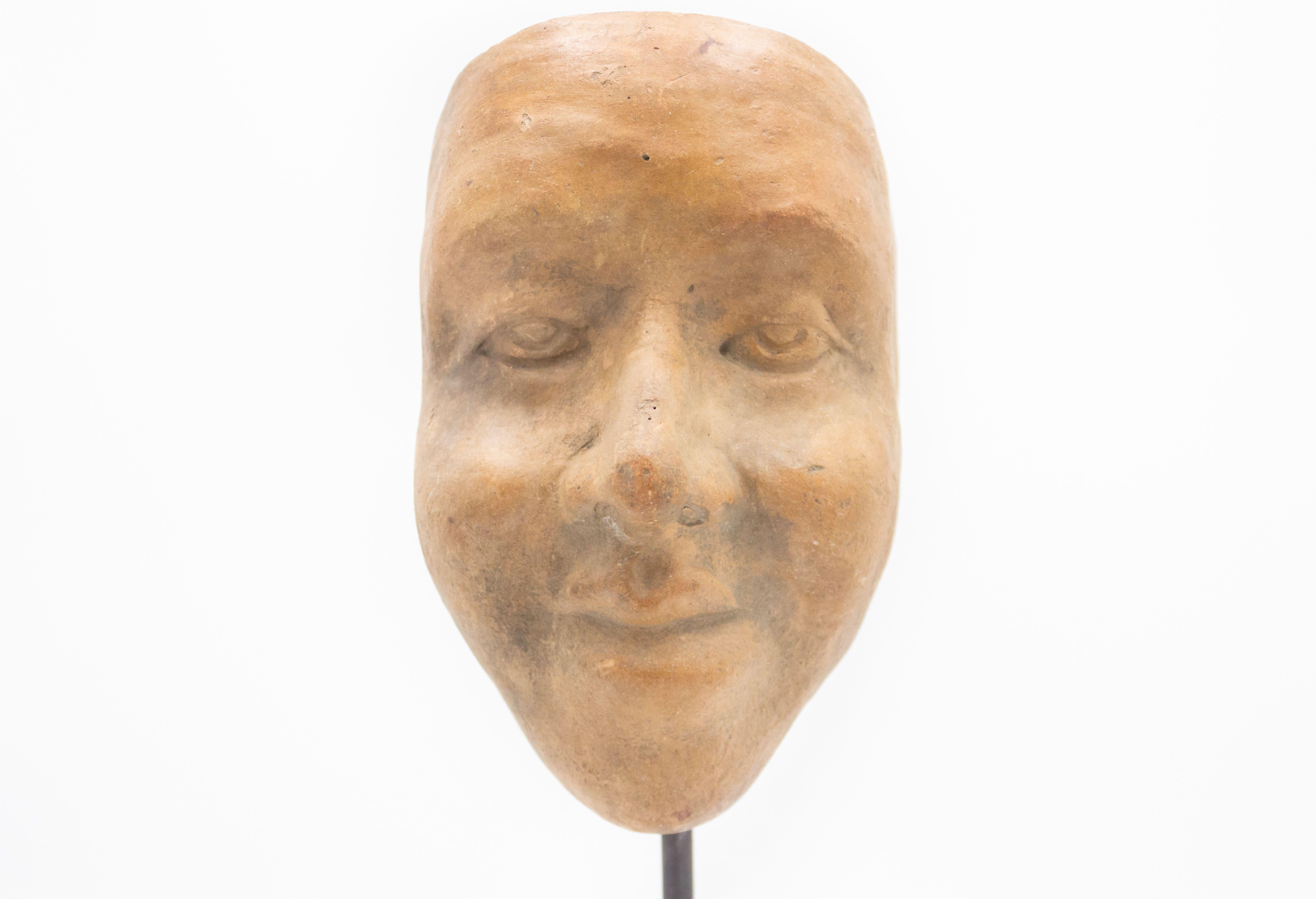 Continental German (late 19th Cent) sculpted terra-cotta master mask mold of a large serene face displayed on a square black marble base stand (part of a collection).
 