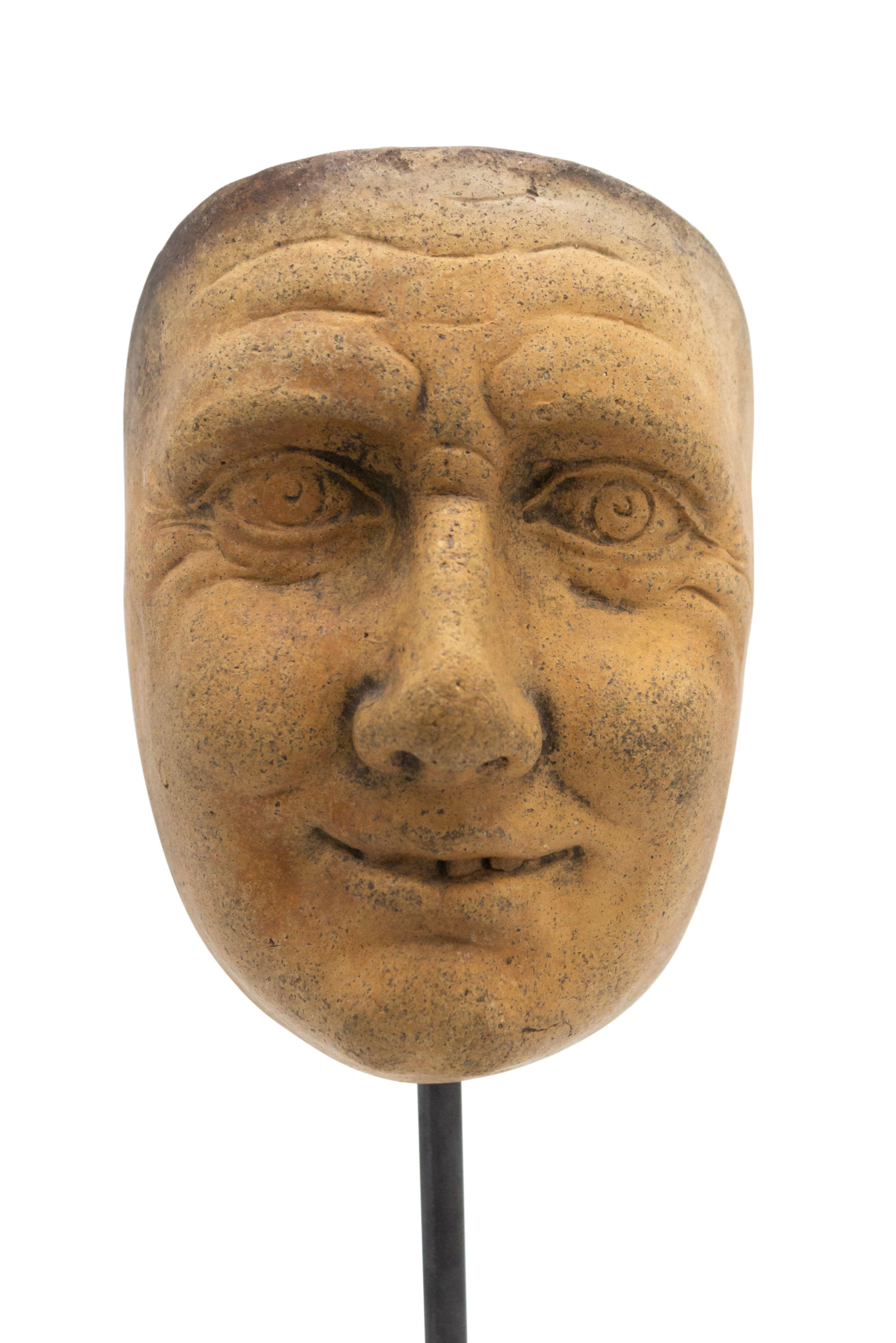 Continental German (late 19th Cent) sculpted terra-cotta master mask mold of a grinning face with intense eyes displayed on a square black marble base stand (part of a collection).
 