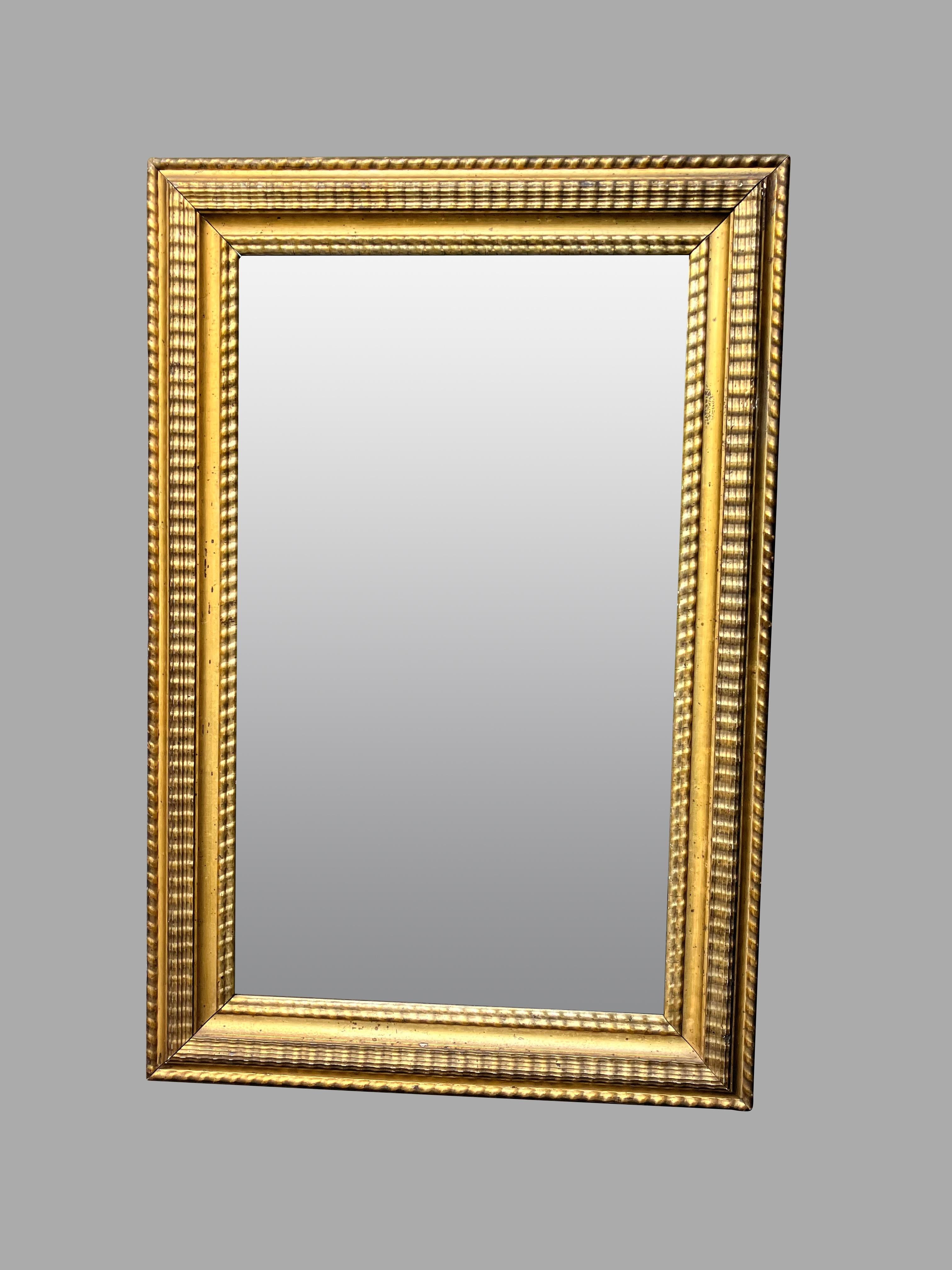 An attractive American giltwood and gilt composition mirror retaining its original glass plate, the frame with a gadrooned and rope form border. This mirror is a useful compact size suitable for a hallway or library. The original glass has an
