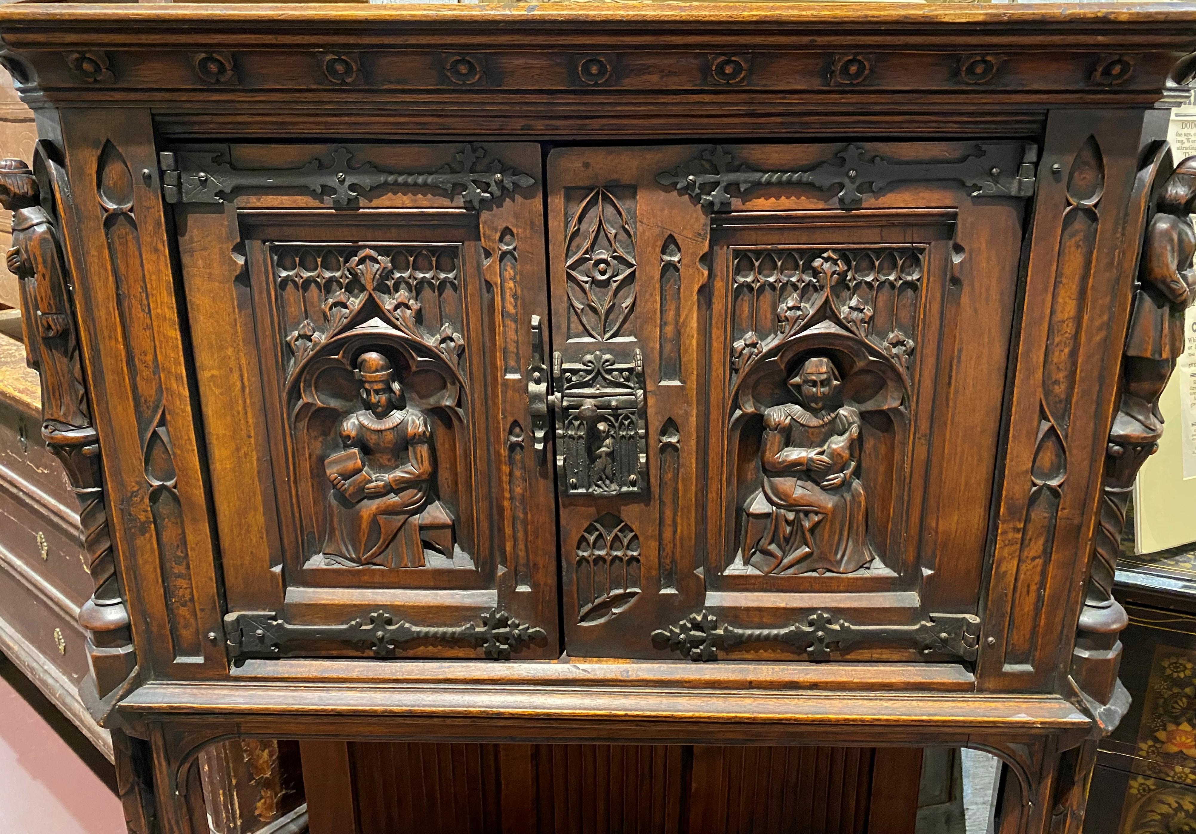 A finely carved Continental Gothic style two-door cupboard or altar, probably oak, with open linen-carved panel back base and sides, the doors featuring a carved figure on each, canted corners with additional carved figures of monks or priests, and