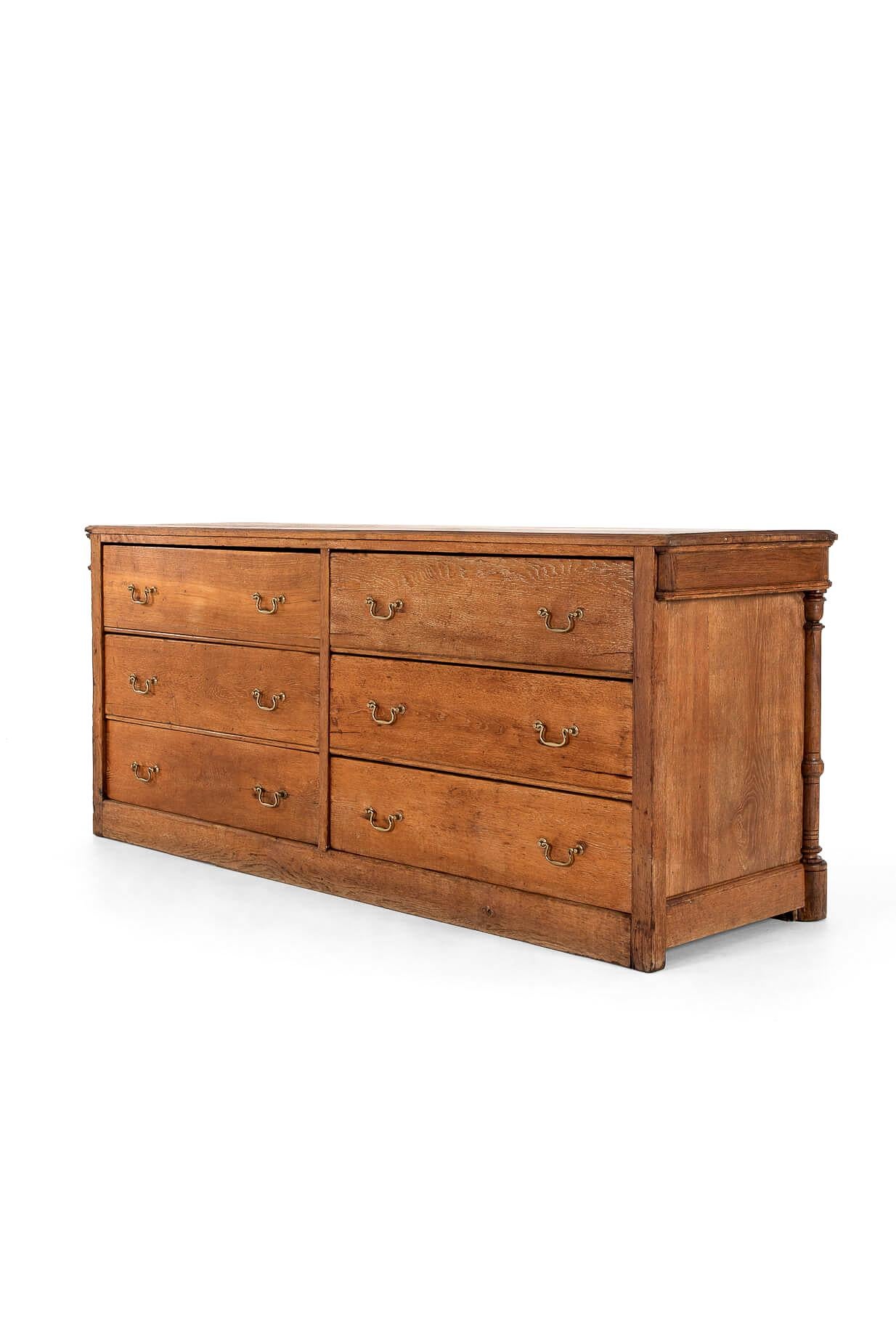 A wonderfully presented bank of haberdashery drawers in limed oak with a generous thick plank top.

Six unusually large smooth-running frieze drawers with original brass loop handles and shapely carvings on both ends, raised on a plinth base.

We