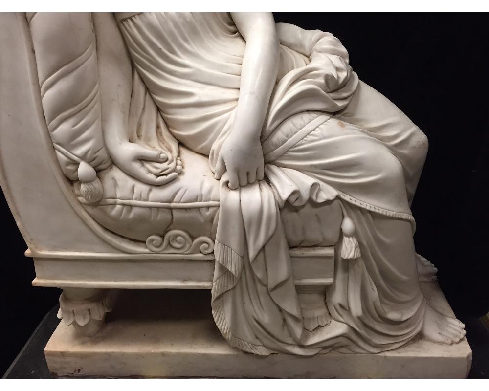 Monumental continental hand carved marble figure of a reclining maiden in classical robes seated on a traditional European recamier cushioned with tassels, all raised on a rectangular marble plinth. 20th century.
Meticulous attention was given to