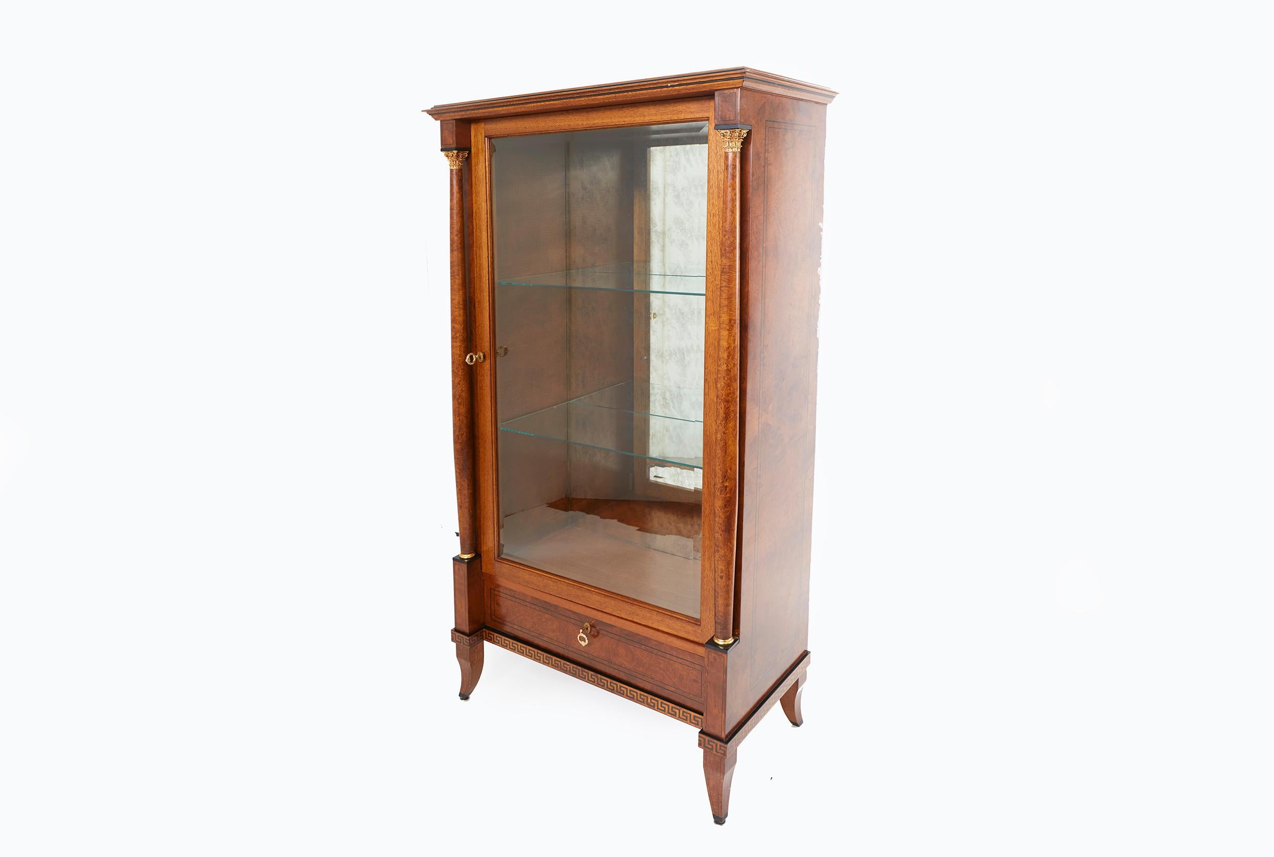 Late 19th century continental mahogany wood with mirrored back and glass shelves display cabinet with gilt laurel wreath as handle, with two Corinthian columns and gilt acanthus detailing. The cabinet featuring a geometrical motif with two glass