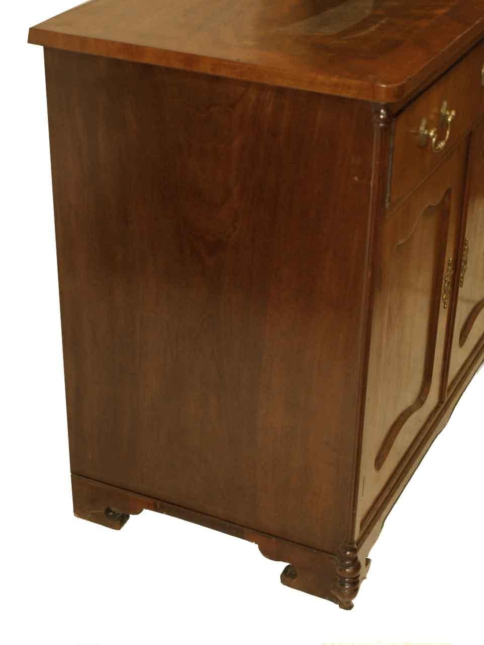 Continental mahogany one drawer cabinet, the top with book match flame mahogany veneer and cross banded edge above pull out brushing slide; single drawer with swan neck brass pulls over double doors with inset panels, interior with one shelf. The