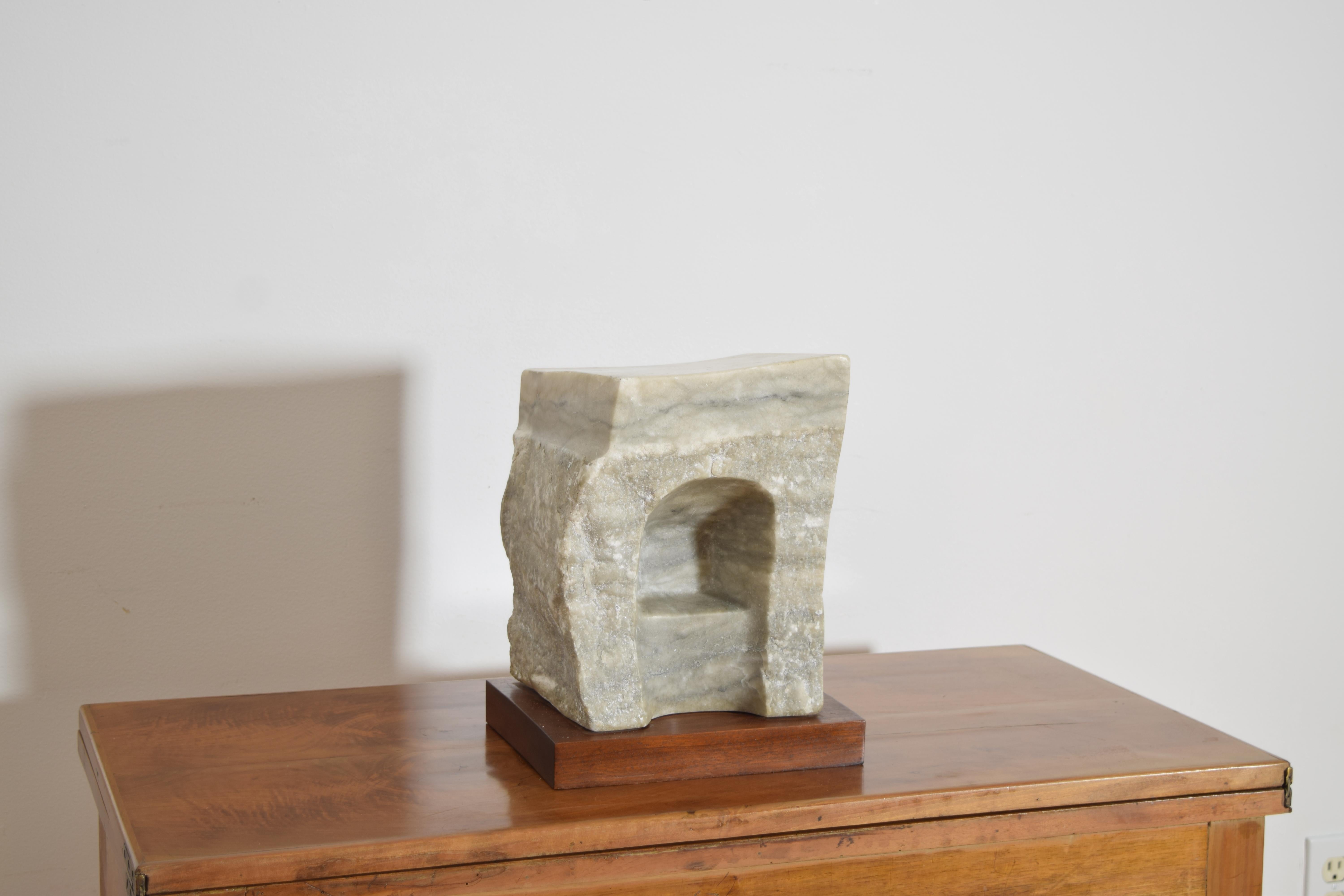 hand-carved stone sculpture with a hewn finish, featuring an arched recess and mounted on a square wooden plinth, marked 