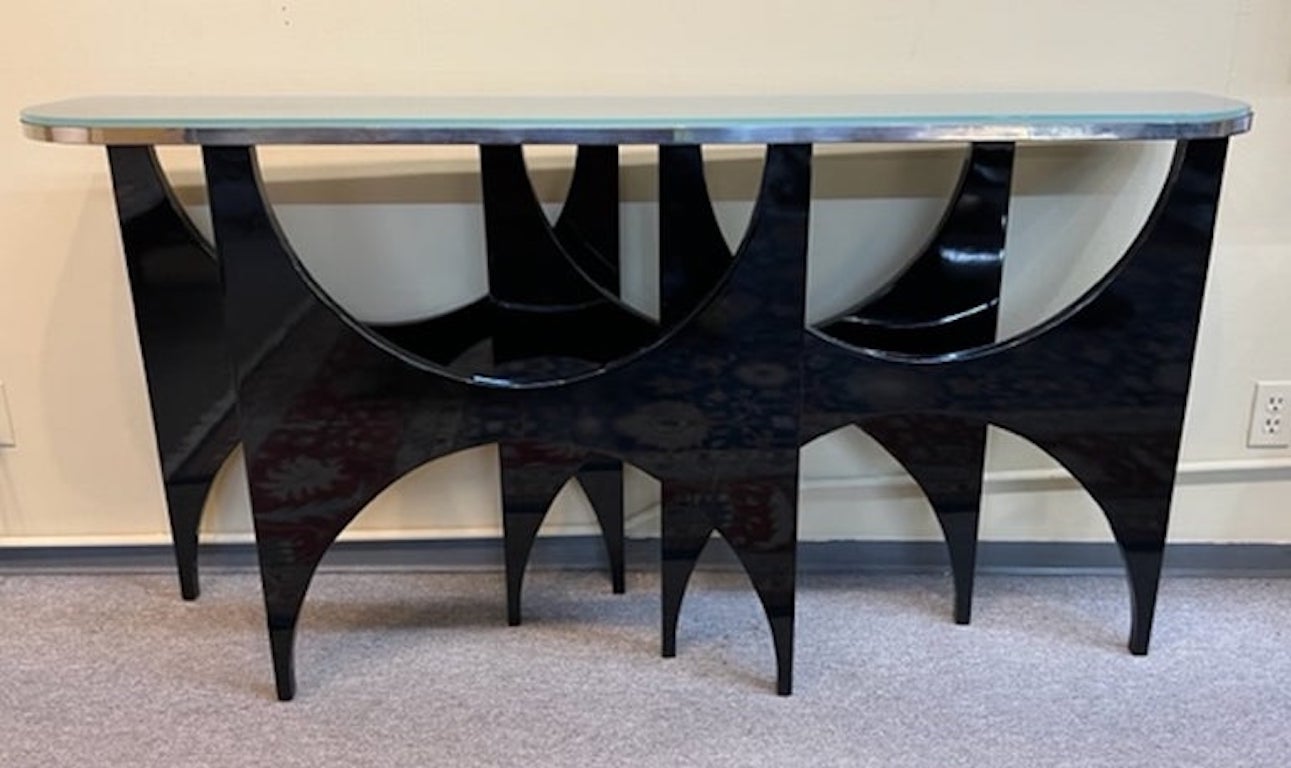 Konsole mit sehr einzigartiger Form und Design. Die Holzplatte ist von einem verchromten Zierelement umgeben. Oben befindet sich ein Glas. Die Konsole wird von 4 dünnen ebonisierten Holzbeinen getragen, die oben und unten halbkreisförmige