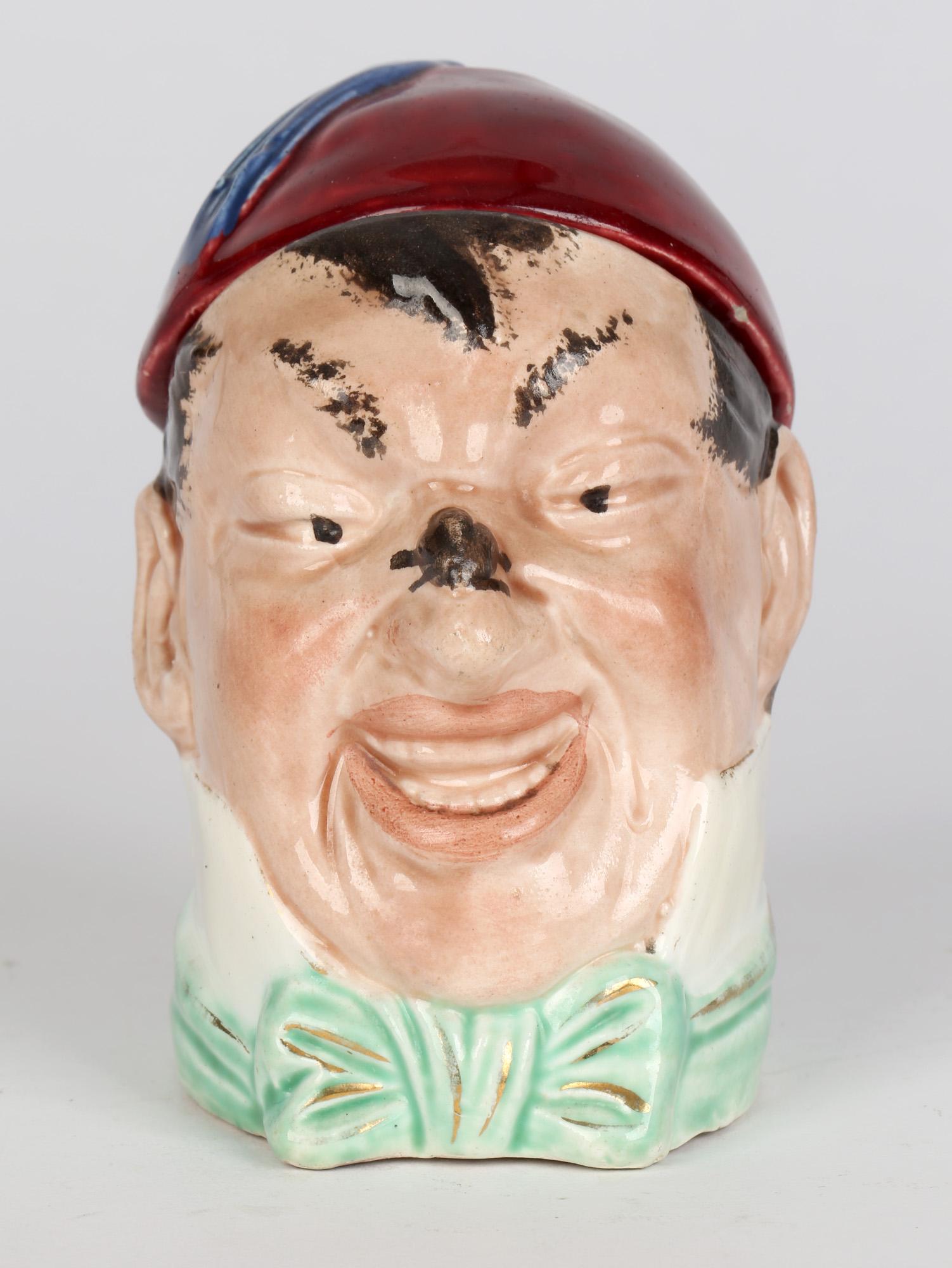 A delightful antique novelty Continental majolica pottery lidded character tobacco jar of a man wearing a fez type hat dating from the latter 19th century. The jar is modeled as the head of a man watching an insect perched on his nose. He is dressed