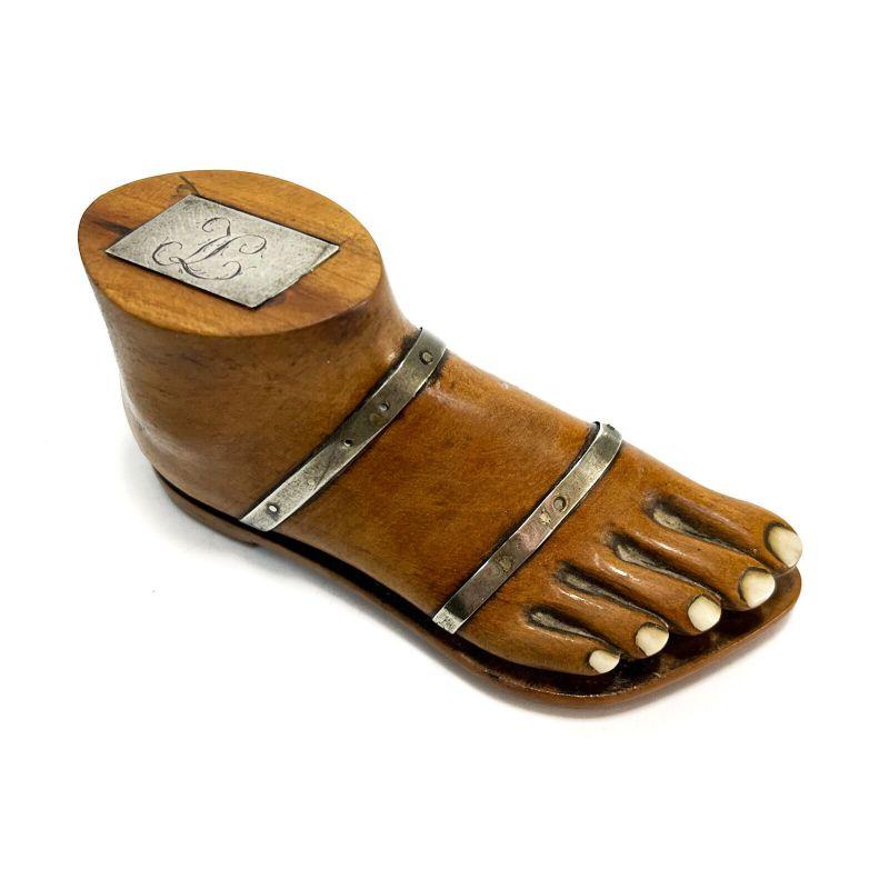 Continental novelty snuff box modeled as a foot, circa 1800.

Carved fruitwood novelty snuff box modeled as a foot with roman style sandal. Silver mounted straps, the toenails set with bone. The underside cobbled with brass and silver. The sandal