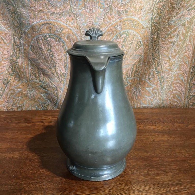 Continental pewter covered jug, the baluster shape with curved spout, the domed lid with a scallop shell thumb piece.
Mark inside lid including “G’SPRENGERS”,
18th century.
