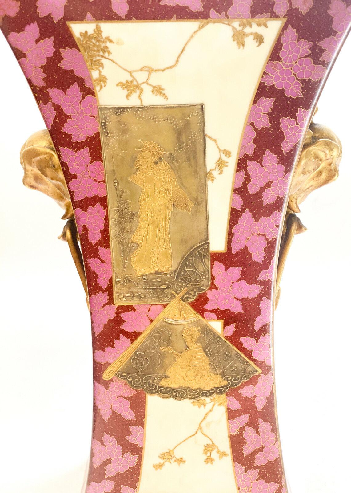 Vase à deux anses en porcelaine continentale japonaise peint à la main et incrusté de dorures

Figures japonaises multicolores en relief et décorées à l'or dans la zone centrale, avec des accents de feuilles sur le fond floral rouge et rose. Têtes