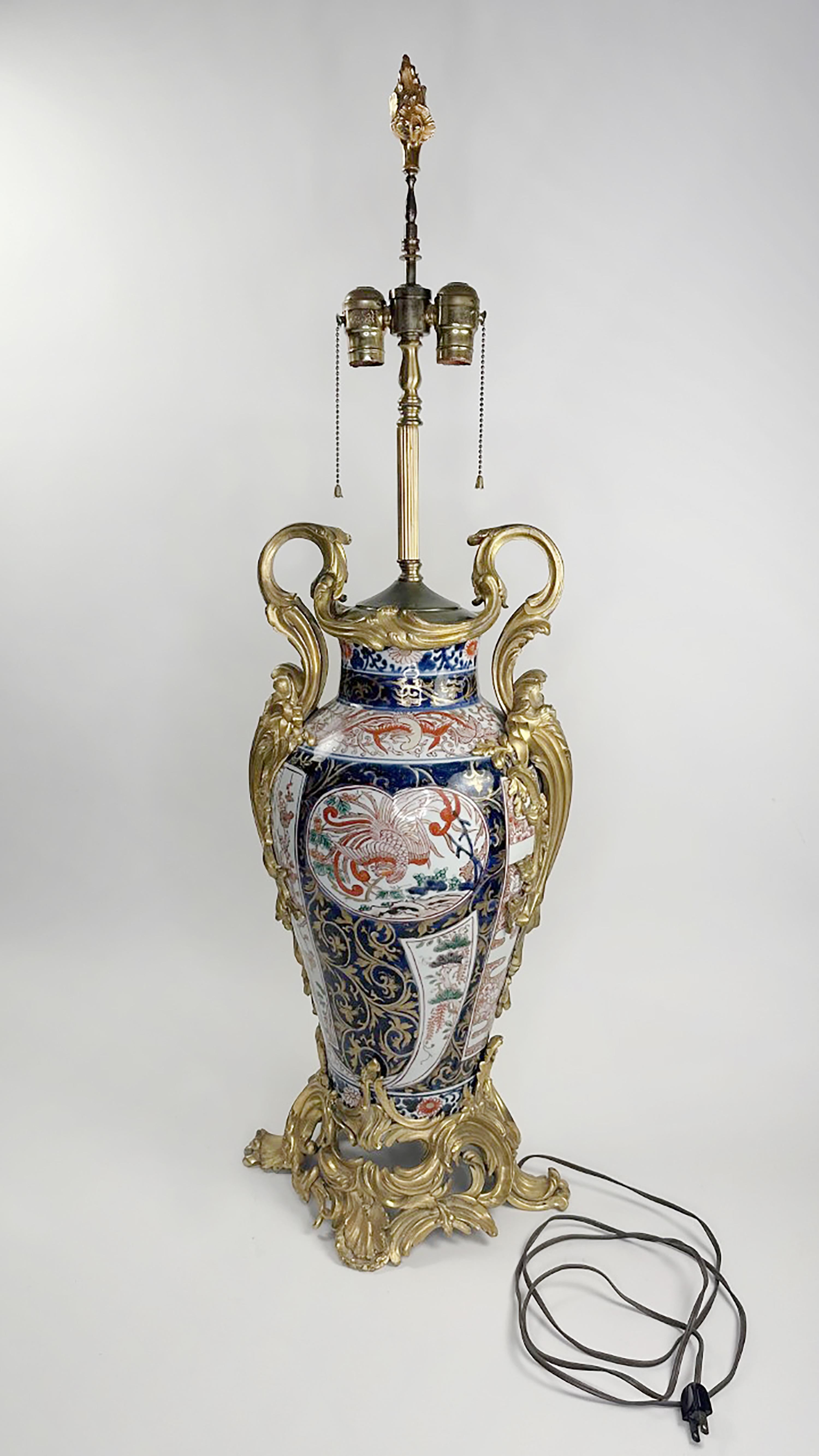 A continental porcelain Imari style urn. repurposed as an Arita-yaki lamp. The center is a wide oval shape. The sides, top, and bottom are ornate with Ormolu detail in lush organic florals. Scrolled double snake handles.  Circa late 19th Century.