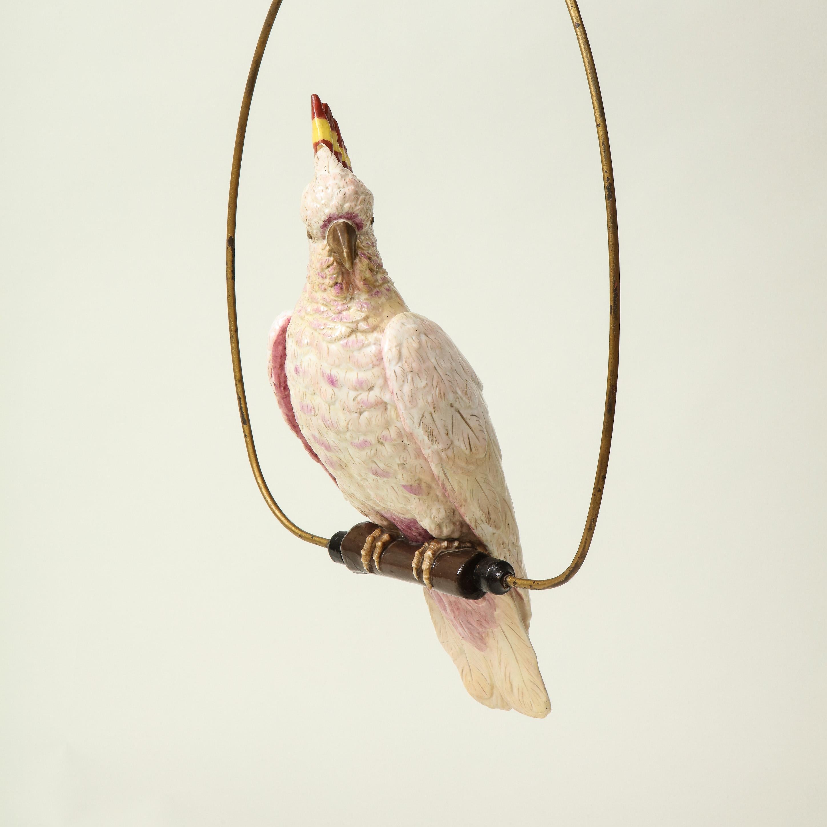 With white and lavender plumage and red and yellow-striped crest; perched on a wooden beam within a metal hoop. Note dimensions include hoop.

Provenance: From the Collection of Mario Buatta, New York, NY.