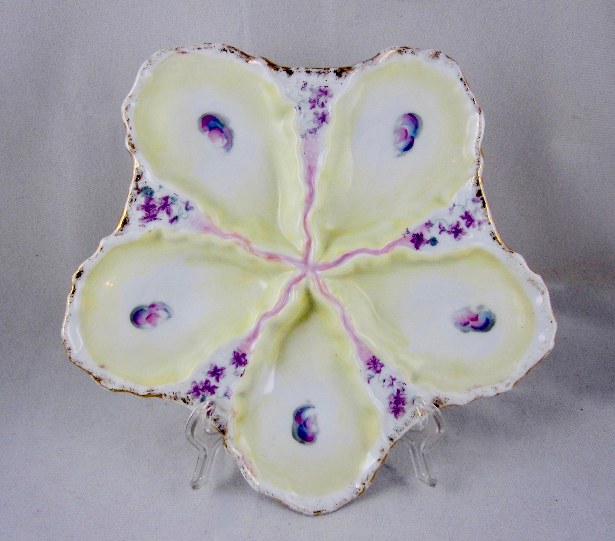 A continental porcelain hand-painted oyster plate, star-shaped with five wells, circa late 19th-century. Each well has a blush of buttercup yellow and an oyster ‘eye’ in its centre. The wells are separated with a floral pattern of small violets.