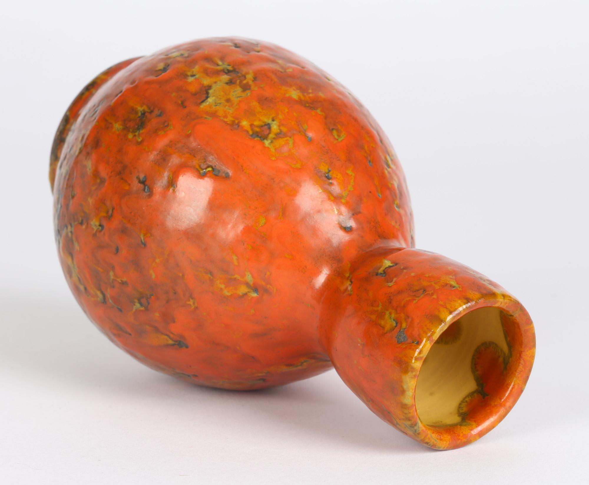 A stylish Continental attributed, possibly German, mid-century art pottery vase decorated in bright orange mottled and textured glazes. The vase made from a terracotta colored clay stands raised on a narrow rounded and unglazed foot, with a rounded