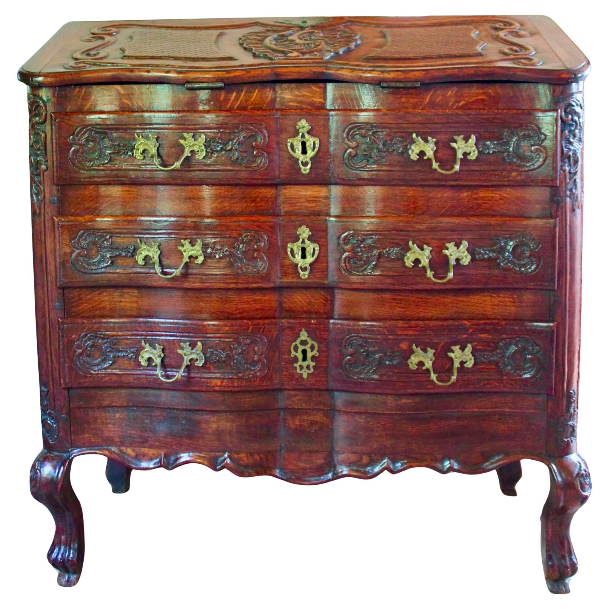 An exuberantly carved antique Northern European desk (probably Dutch) of unusual form: a serpentine block front case piece with three drawers and a slightly sloped fall front lid above, designed to be supported by the drawer below. The carving is