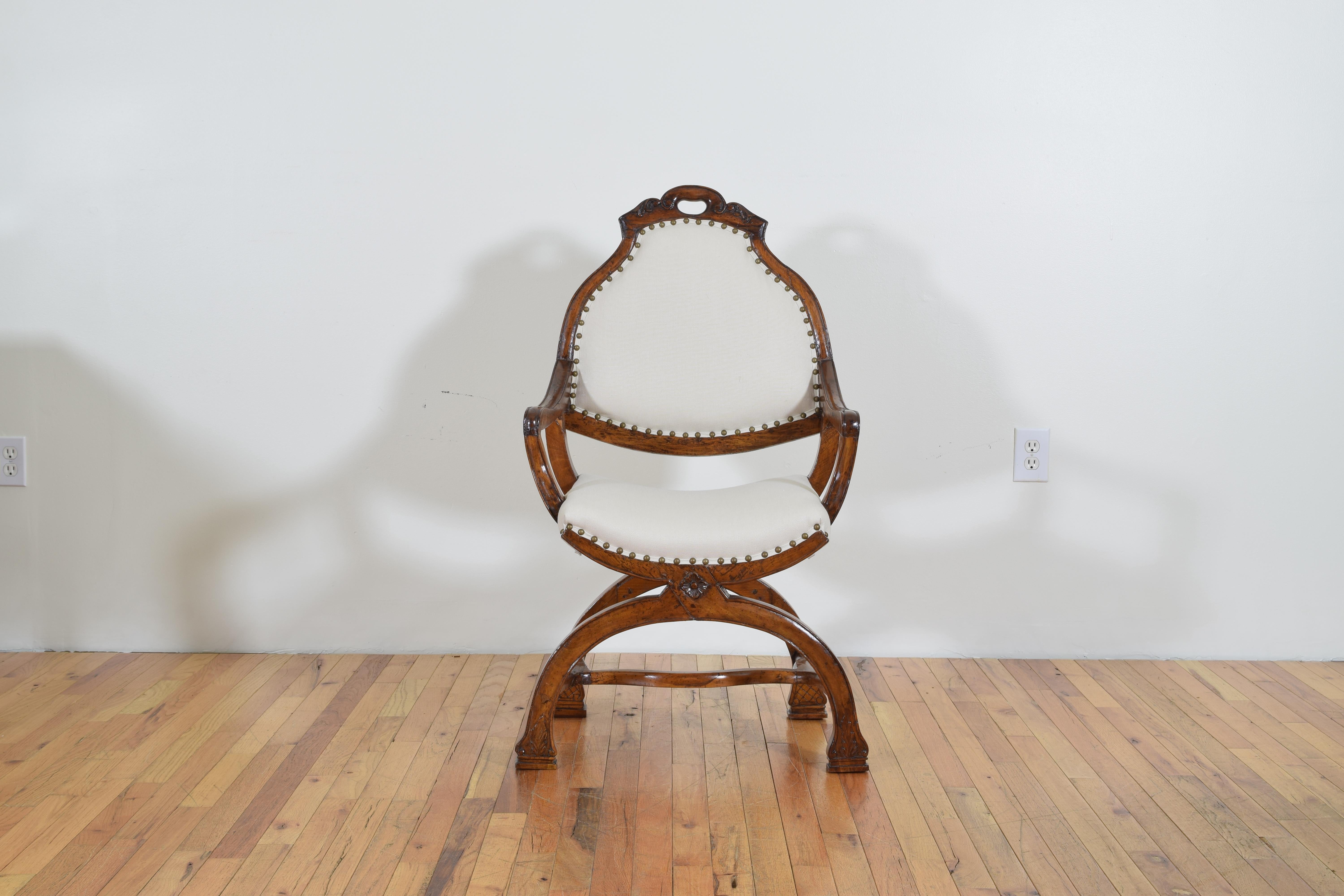 Having an arched and handled backrest atop open arms, the shaped fitted seat of Curule form above reverse arched legs joined by a shaped stretcher.