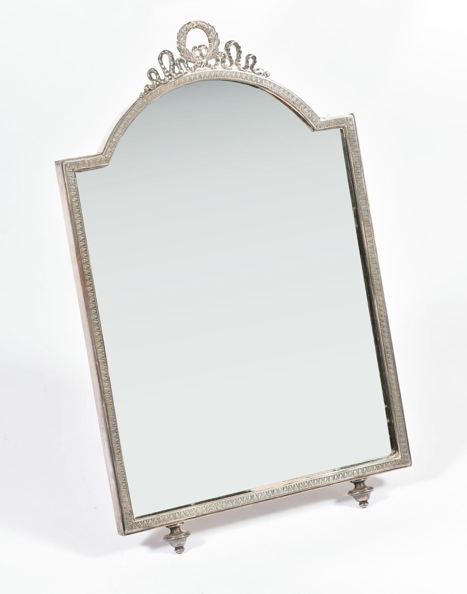 Decorative silver plated dressing table mirror with patterned frame, scrolled top and shaped feet. Sits on easel back. Marked BM G.