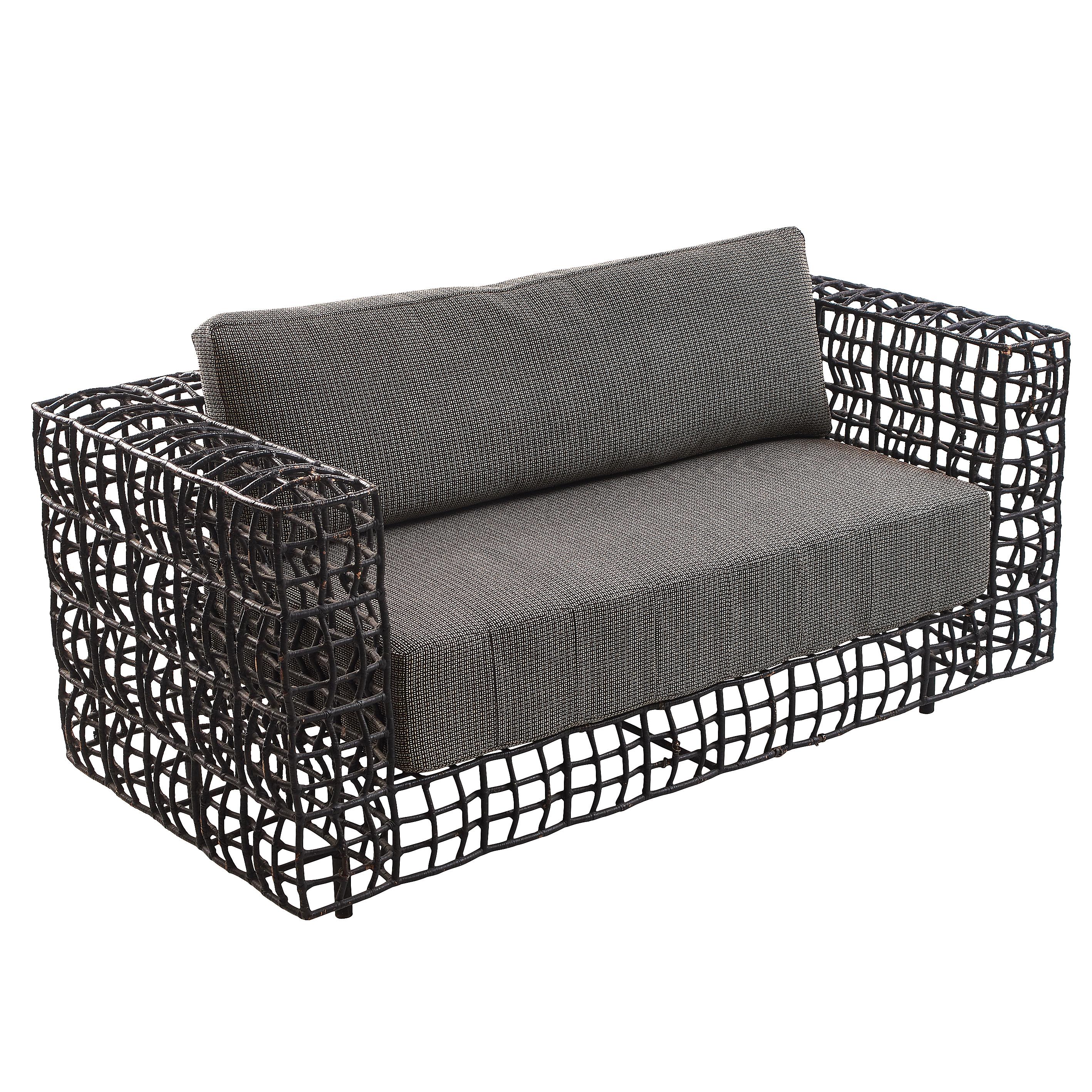 A Continental living room set consisting of a large, 1960s sofa and matching armchair. Each with a steel lattice work frame, wrapped in black painted wicker, with wide arms and later grey cushions, that have been shaped to mirror the 