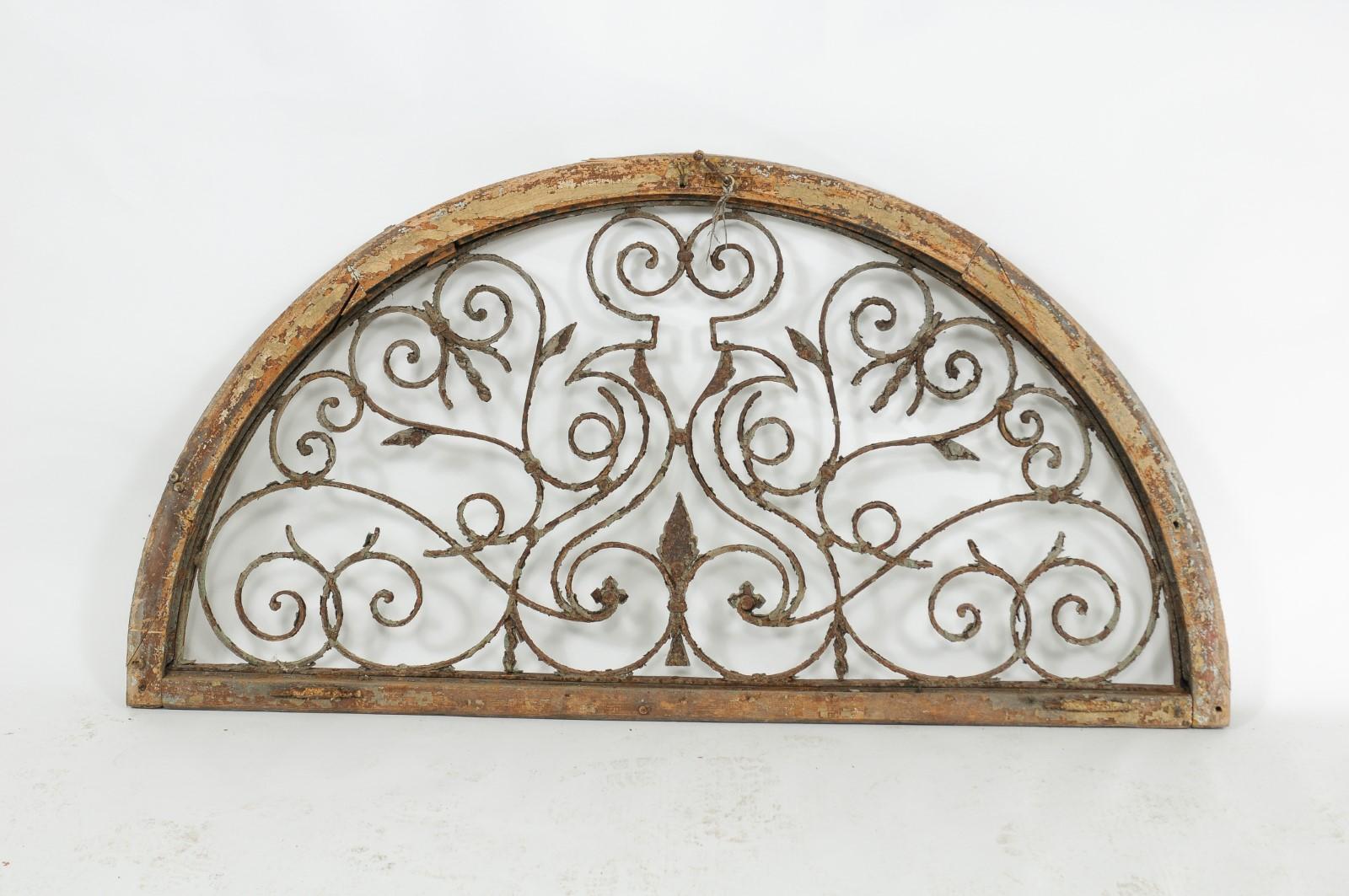 A continental wrought iron and pine decorative demilune architectural wall panel from the Turn of the Century with arabesques of scrolls, volutes and weathered patina. Born in the very early years of the 20th century, this interesting architectural