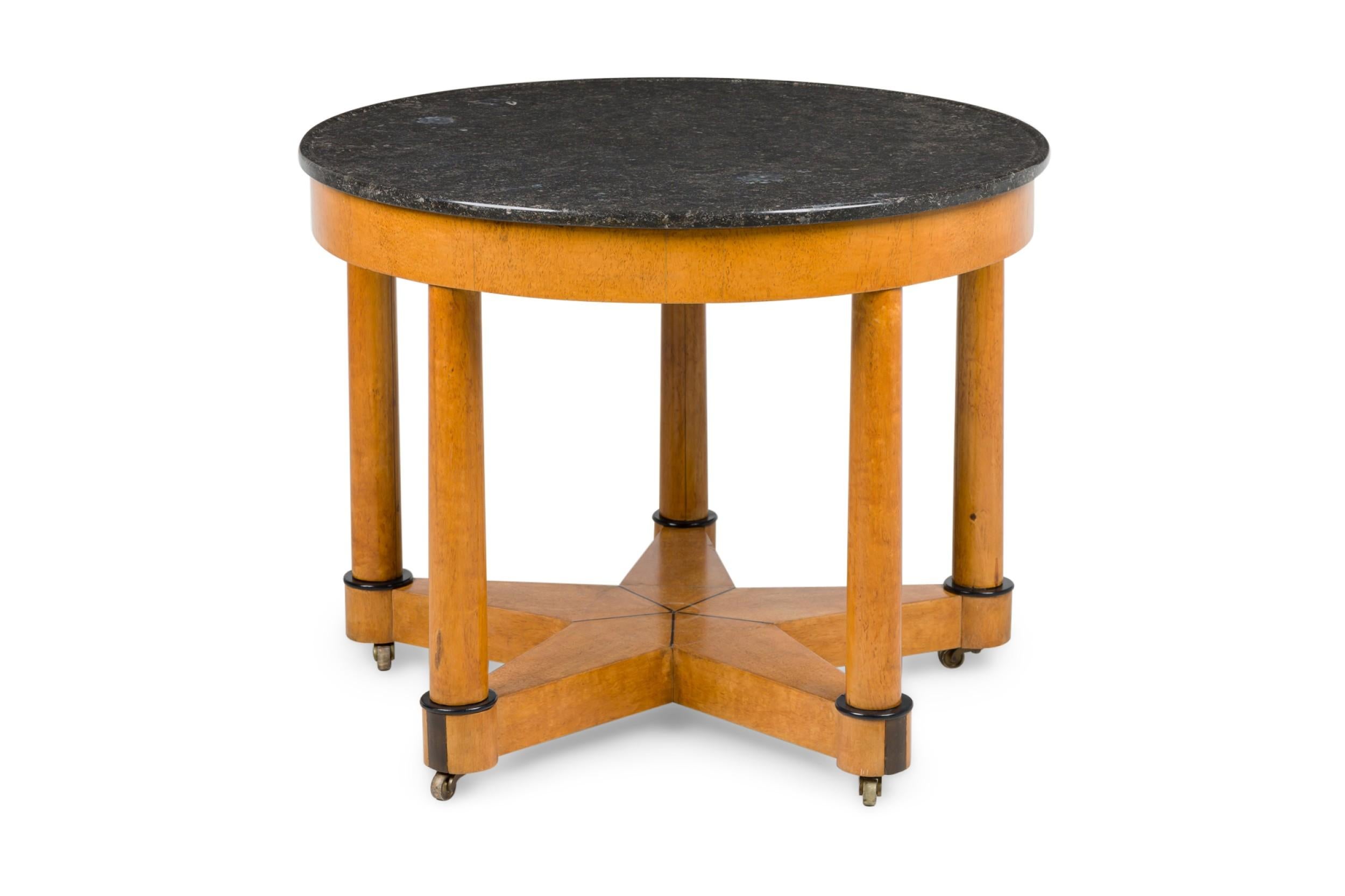 Biedermeier style (Mid-Century) birch rounded center table with 5 legs with casters that create a star shape stretcher with ebonized trim at base and having a round black marble top