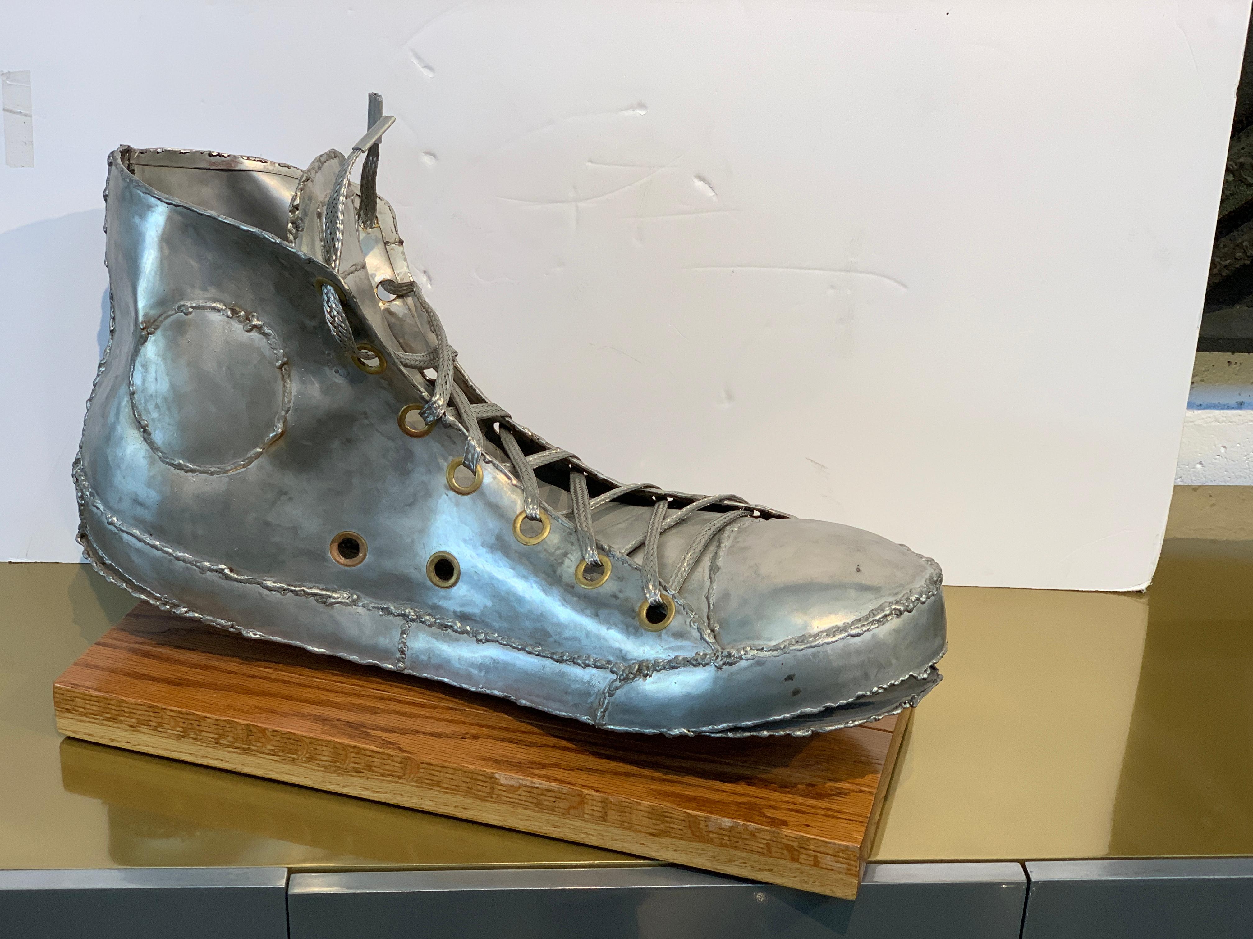 A marvelous sculpture of a Converse Chuck Taylor sneaker in Aluminum(?) or metal. A magnet does not adhere. It is hand welded or soldered and is monogrammed on the tongue, which is pictured. The sculptured is mounted on an oak base. The sculpture
