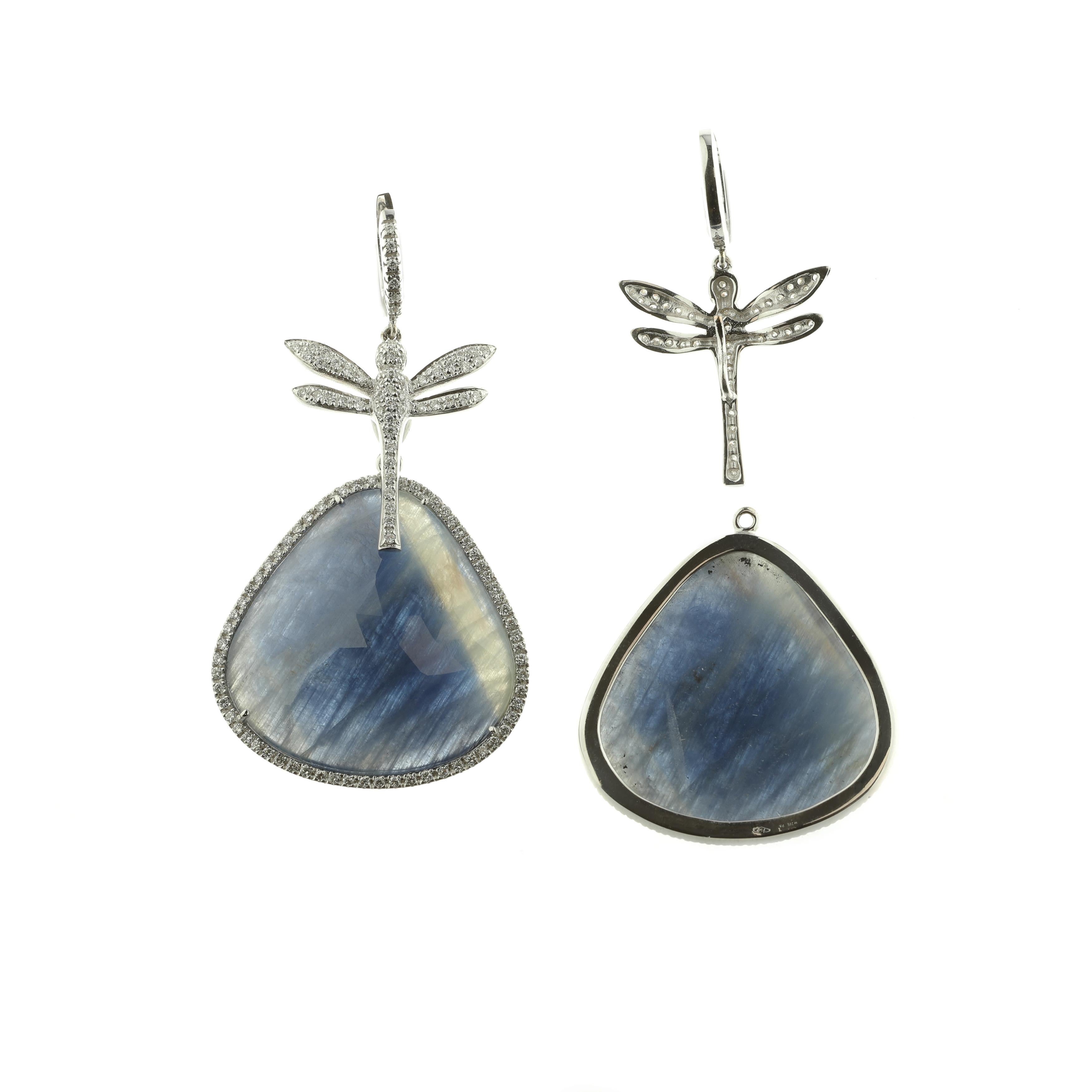 A stunning set of earrings masterfully created entirely by hand feature an 18-karat white gold hoop and dragonfly, both pavé-set with white diamonds. A spectacular, large blue sapphire framed in white diamonds is suspended below (62 carats total).