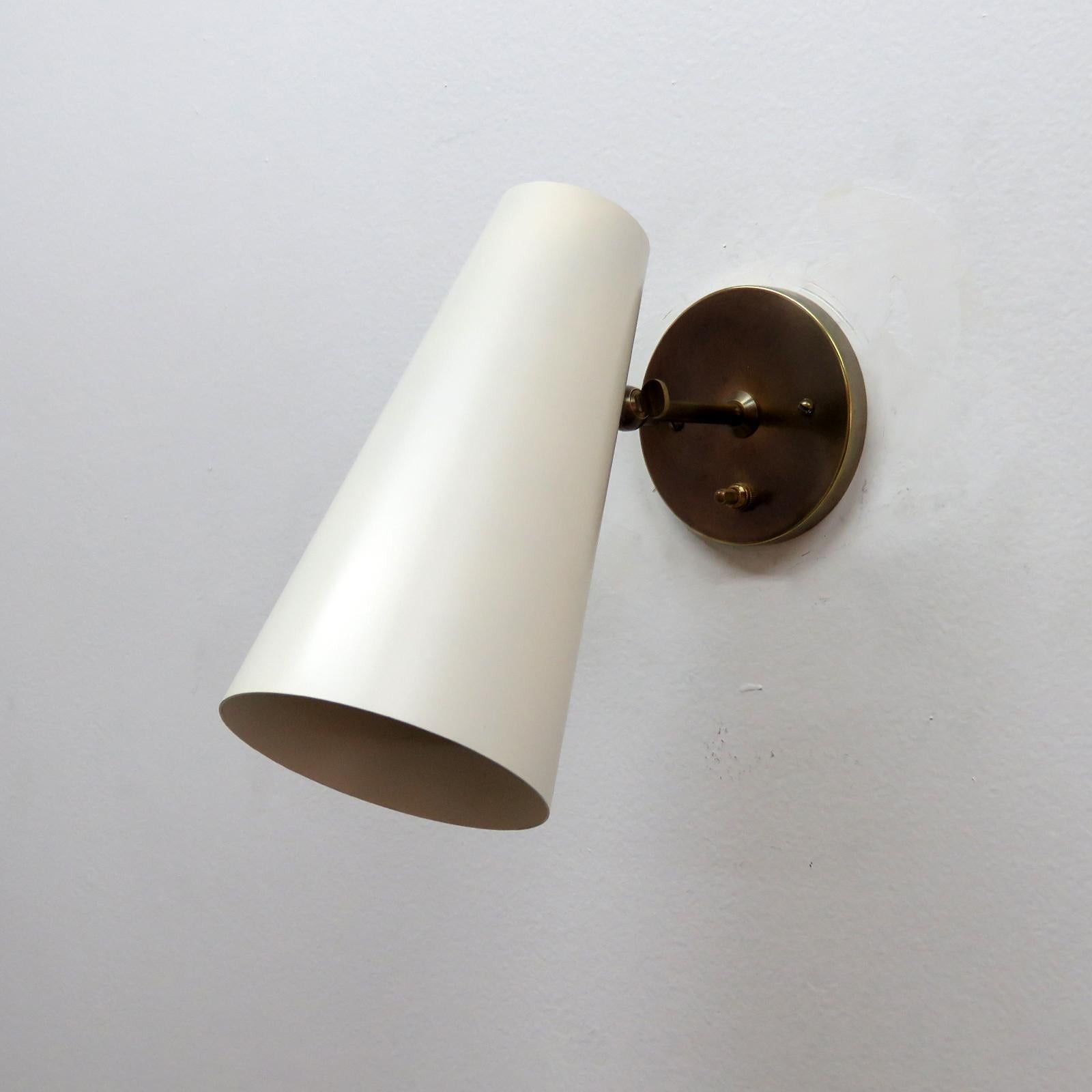 Elegant articulate 'Copa' wall lights designed by Gallery L7, handcrafted and finished in Los Angeles from American brass with an eggshell colored cone on aged brass hardware, the angle of the cone can be adjusted, individual on/off switch on each