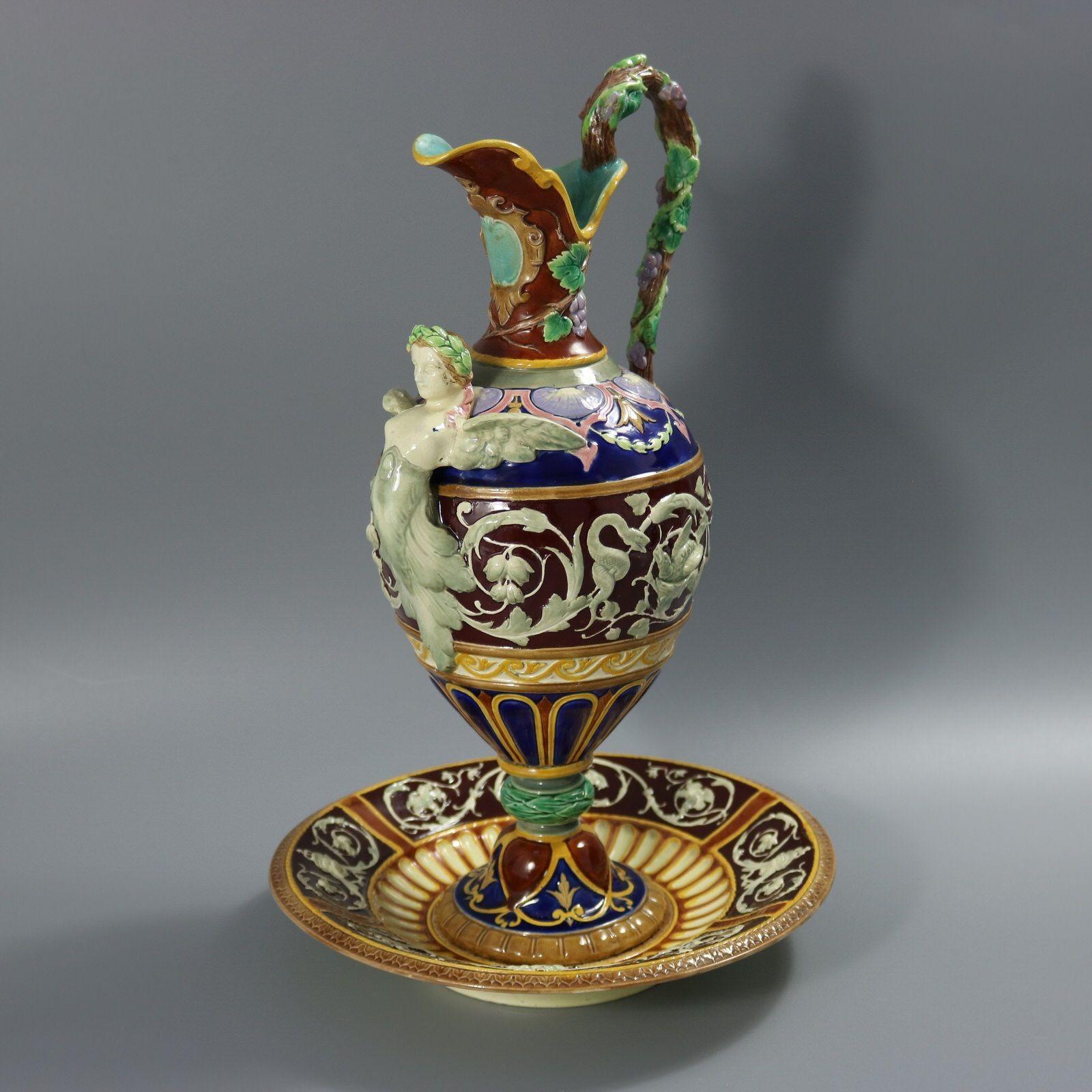 Calice e supporto in maiolica di Copeland con una fanciulla alata sul davanti, uccelli, serpenti, fogliame e frutti di vite decorano i lati e i manici. Colorazione: predominano il marrone, il verde e il blu cobalto. Il pezzo reca i marchi del