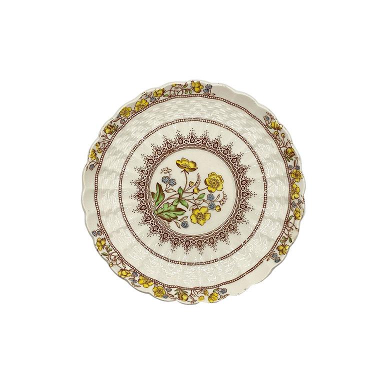 A set of 11 bread and butter plates by Copeland for Spode. This set features 11 round plates with a yellow, blue, and green floral pattern on a cream background. A basketweave design surrounds the rim, while the edges are scalloped. Three of the