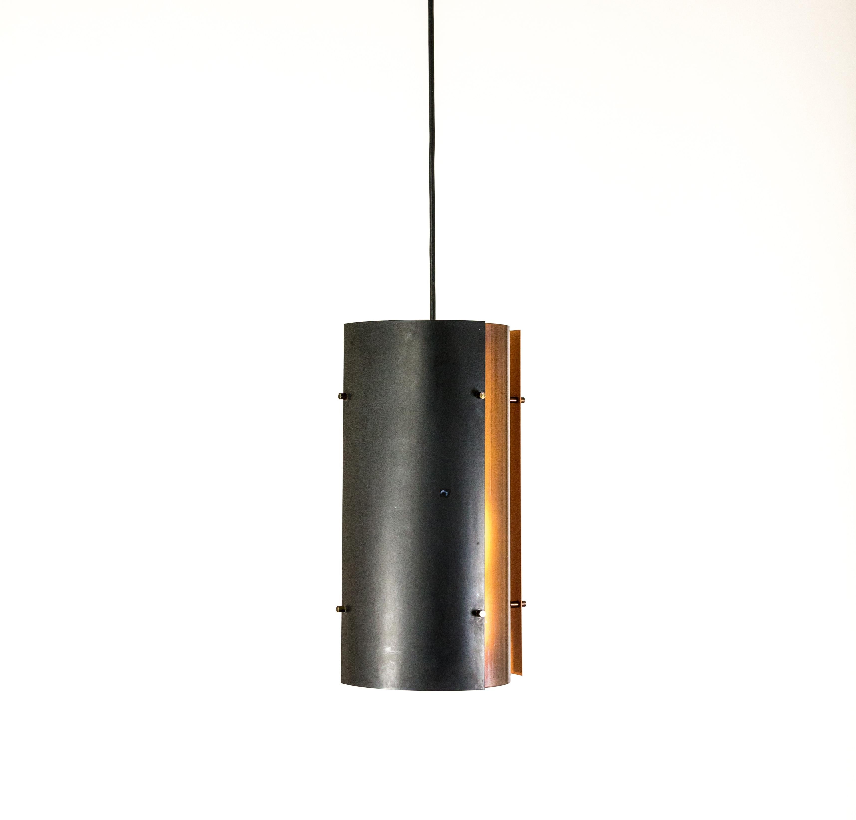 Copper and black colored pendant by Fog & Mørup. The lamp consists of four segments: two black ones with orange on the inside and two copper colored pieces which are white on the inside.

The designer is unknown but the combination of colors and