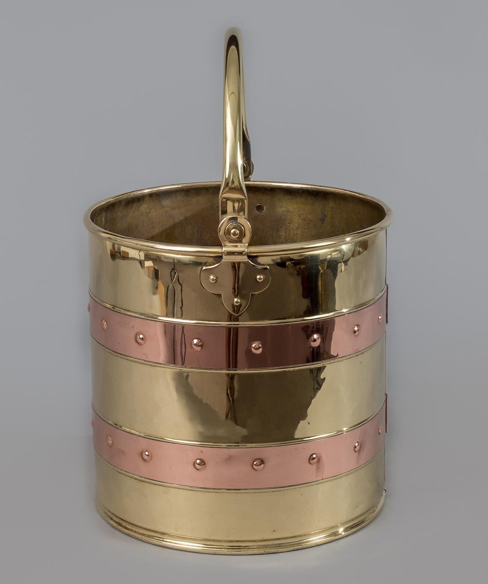 Brass coal bucket with two riveted copper staves, the brass handle attached at the side by a fleur-de-lis shaped mount. Great for kindling.