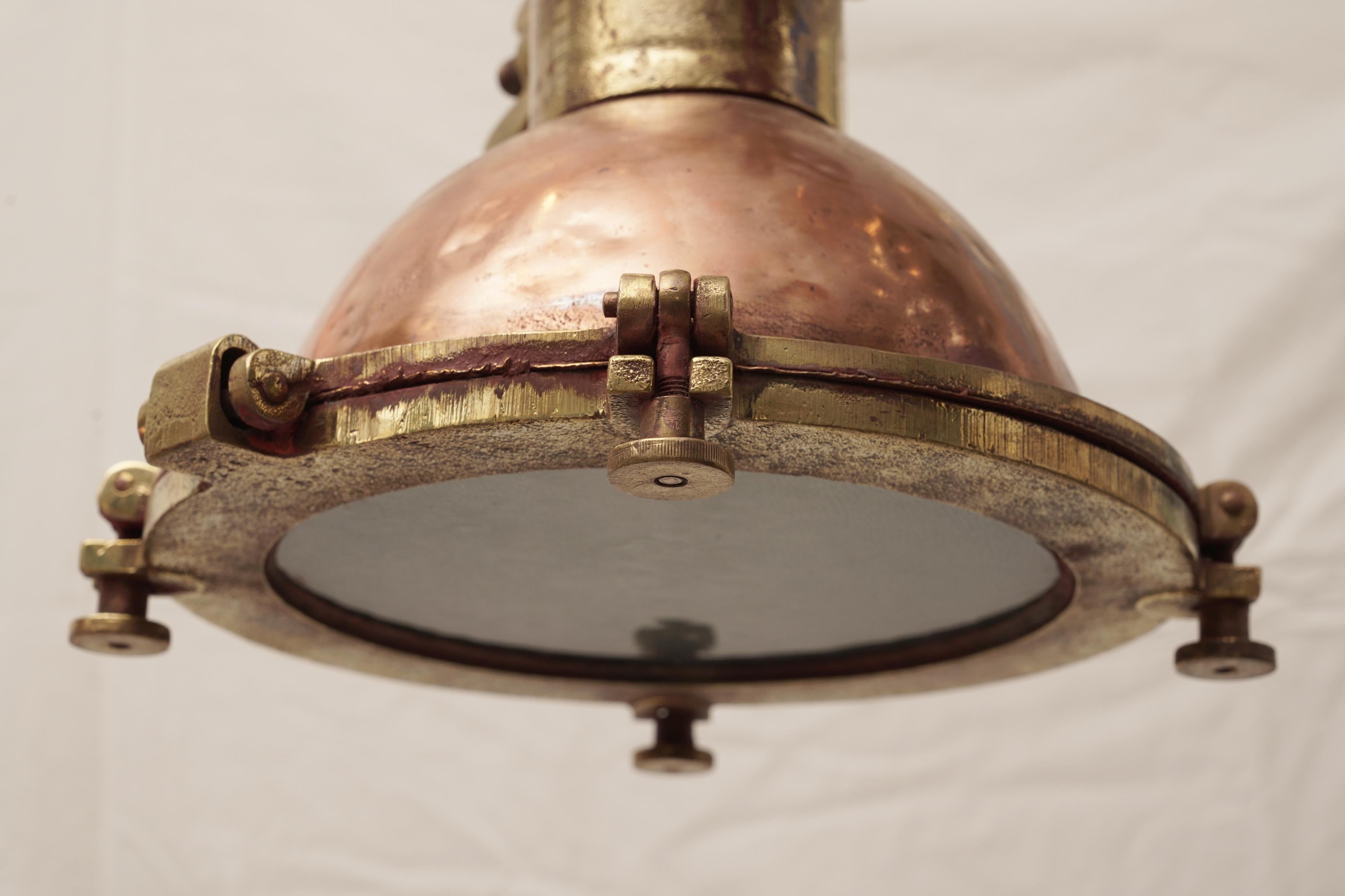 A copper and brass deck light used on ship's to load and unload cargo at night. Hinged face plate and brass pivoting threaded devices (known as dogs) that releases the face plate for changing the light bulb.  The inside has reflective paint  which