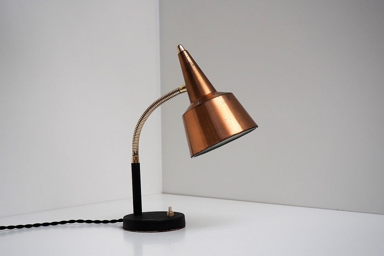 Copper and brass table lamp with black base in the style of Danish Lyfa made in the 1950s.

The shade is decorated with a hole pattern that appears beautifully when the light is on. The shade is mounted on a brass flexible arm, which makes it