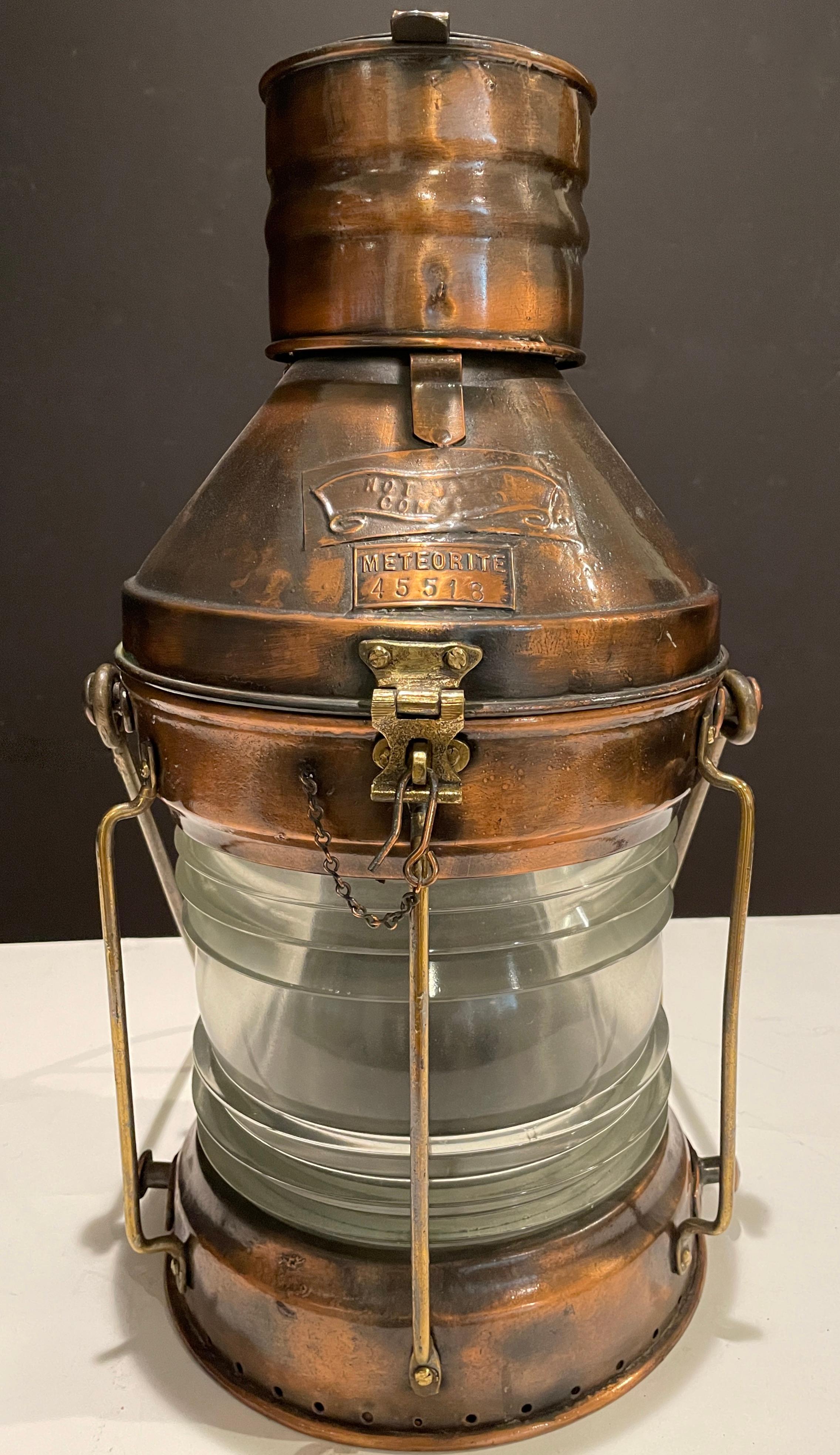 Massive late 19th century copper and brass ship's lantern by the English firm Meteorite. With copper maker's badge, fresnel glass lens and brass bail handle. Massive copper ship’s masthead lantern has a hinged top, brass badges and carry handle.