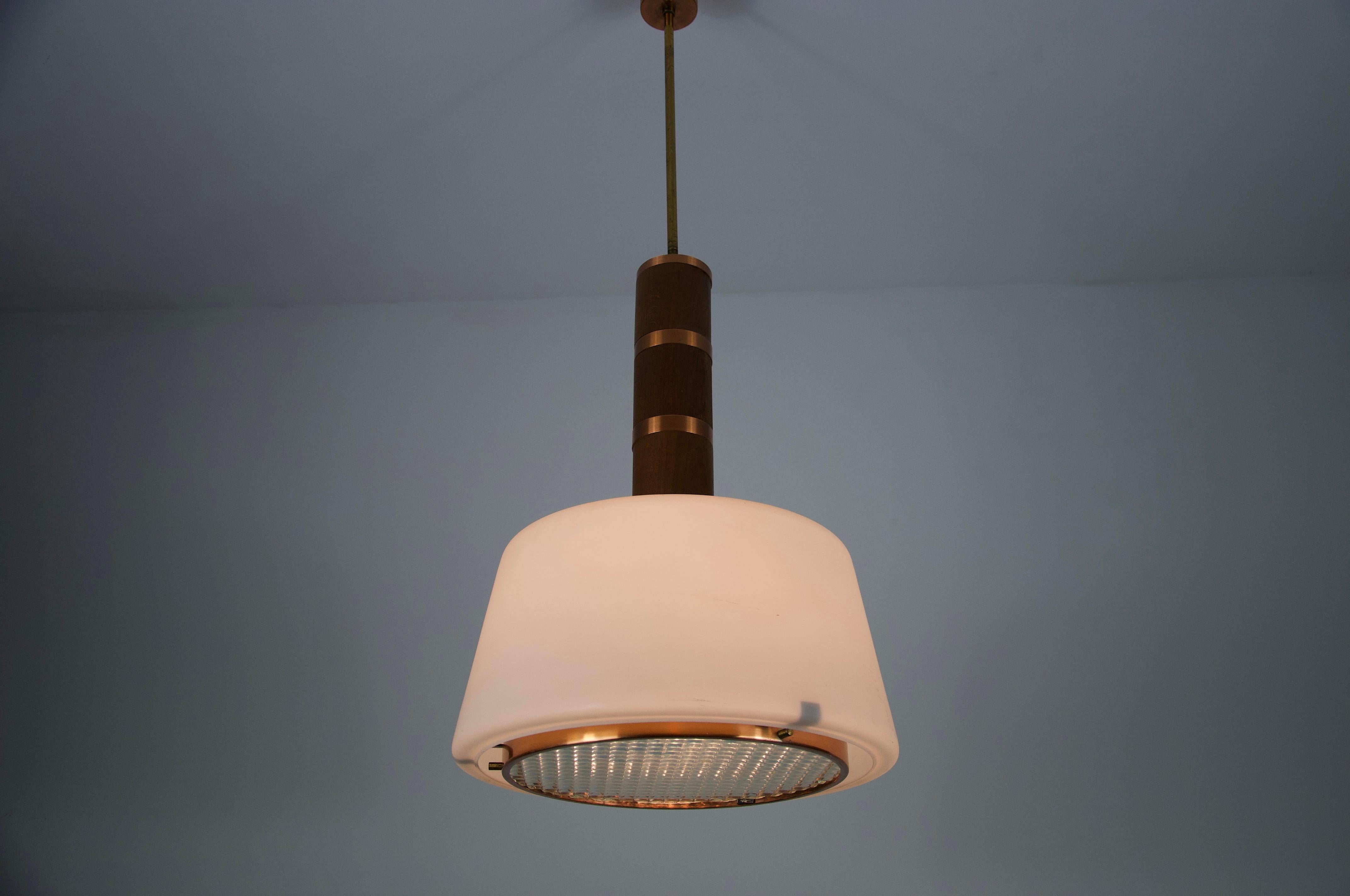 Questa sorprendente lampada a sospensione della metà del secolo scorso, proveniente dall'Italia degli anni '60, combina magnificamente legno, rame e vetro in una composizione raffinata ed equilibrata. Il corpo cilindrico della lampada, realizzato in