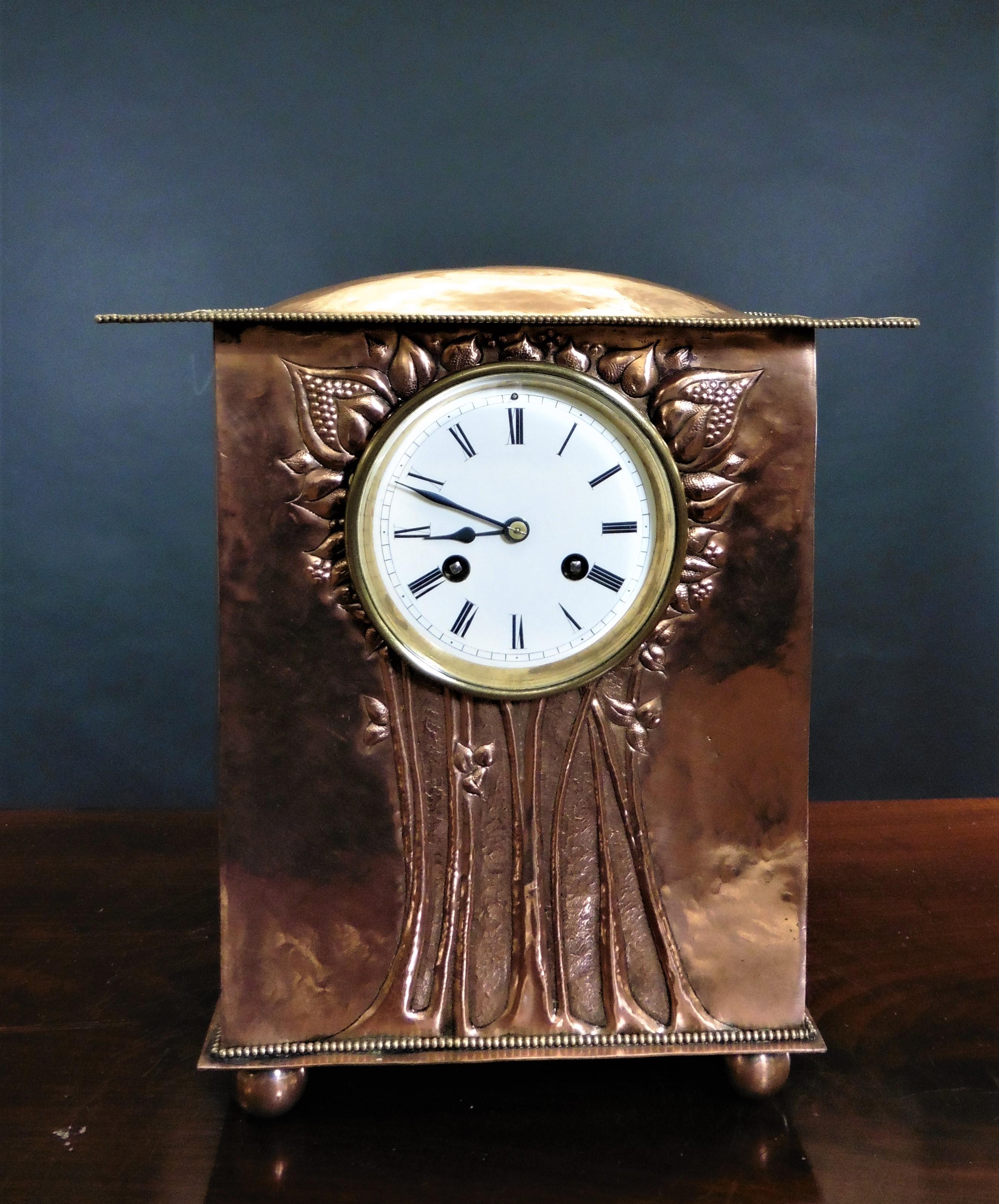 Copper arts and crafts mantel clock Arts and Crafts mantel clock housed in a copper case with domed outswept top with beaded decoration resting on a beaded plinth with four copper ball feet. Unusual decoration to the front of the case depicting a
