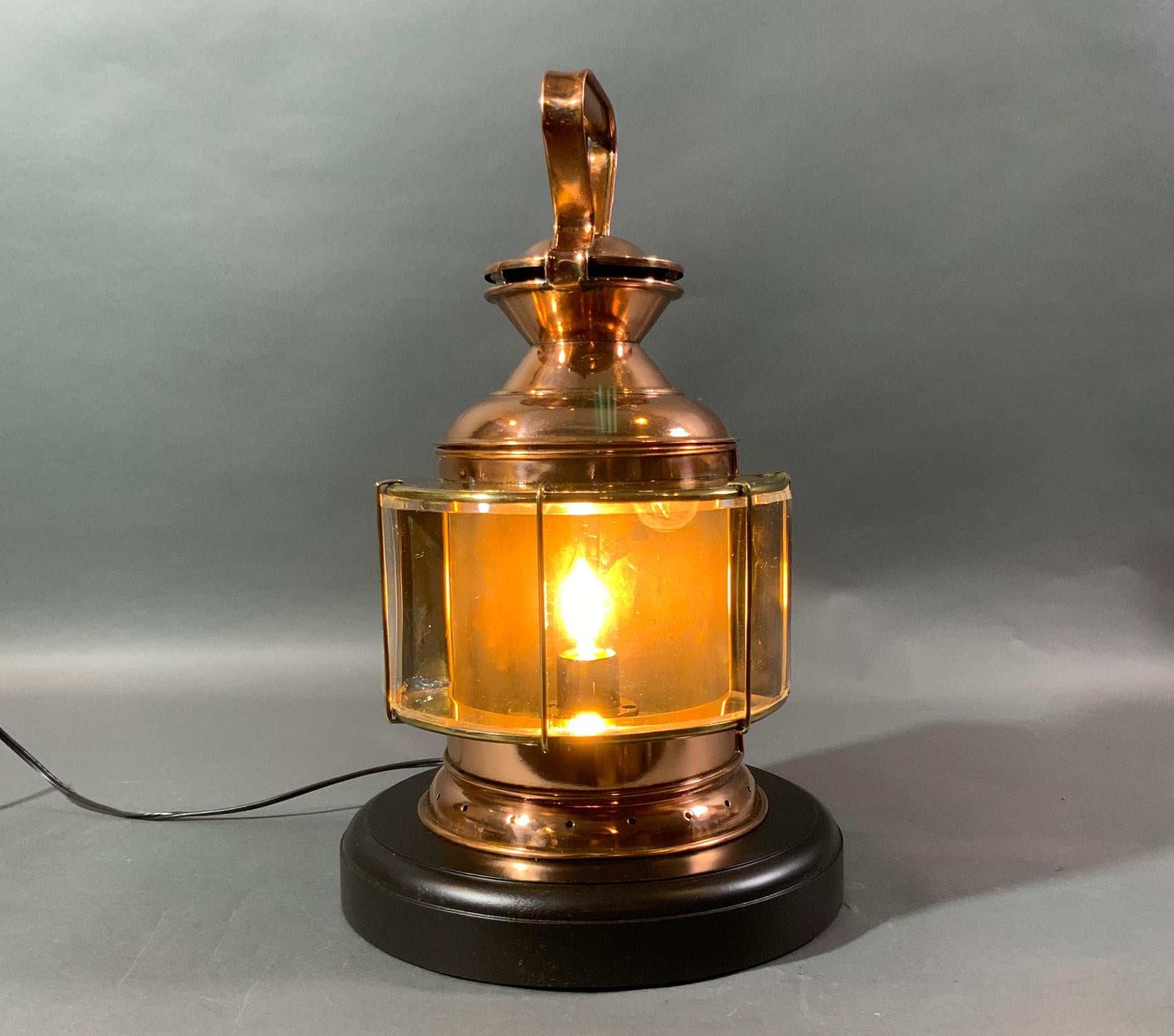 Solid copper signal lantern with curved Perspex lens with brass bars. Copper carry handles. Mounting flange on rear. Mounted to a thick mahogany base. Lantern has been fitted with an electric socket and wire for home use. Thought to be of French