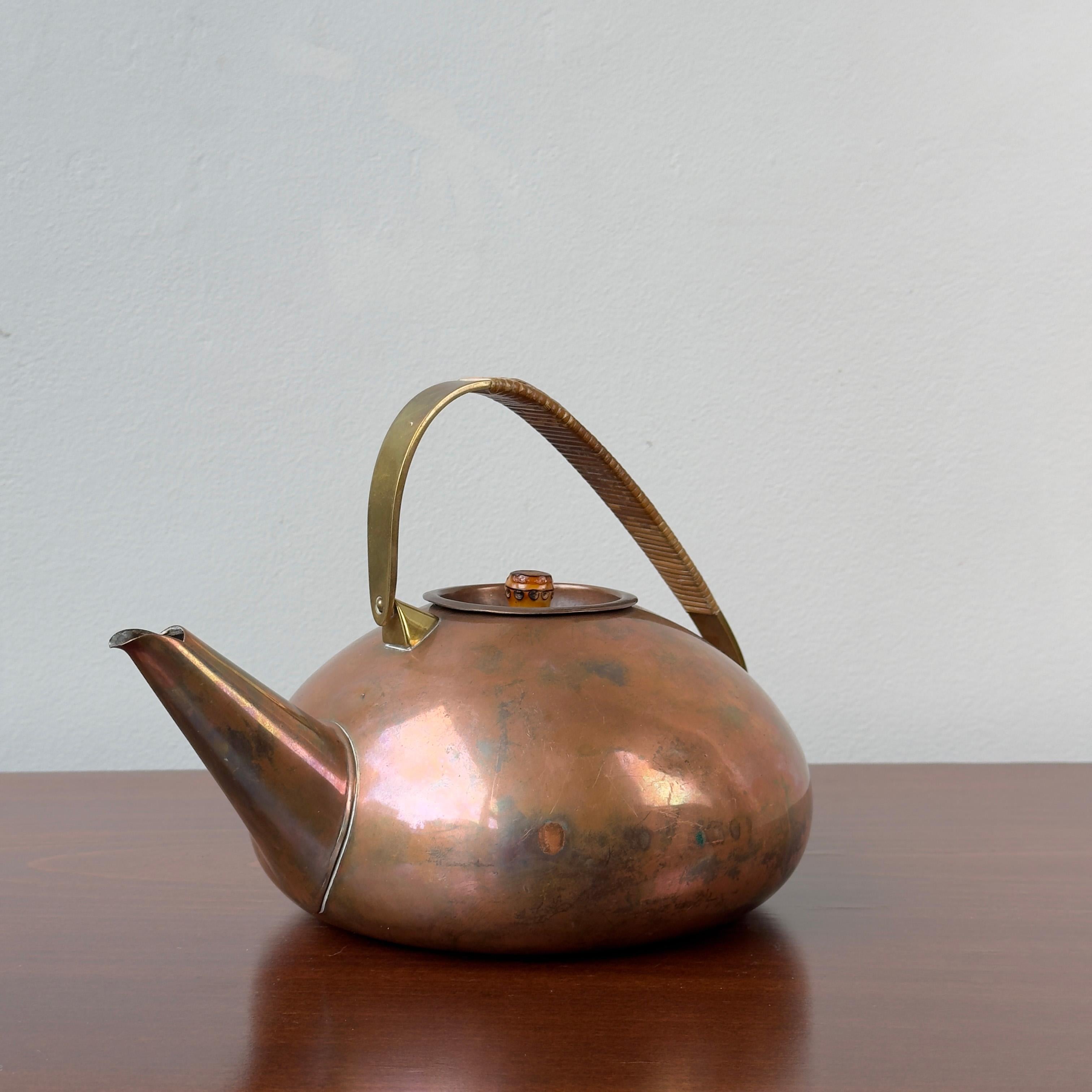 A copper teapot with a cane wrapped brass handle, designed by Carl Auböck II during the 1950s. 

This angular copper teapot was designed by the 2nd Carl Auböck during the 1950s, and like many of his designs, the function led elegance of this piece