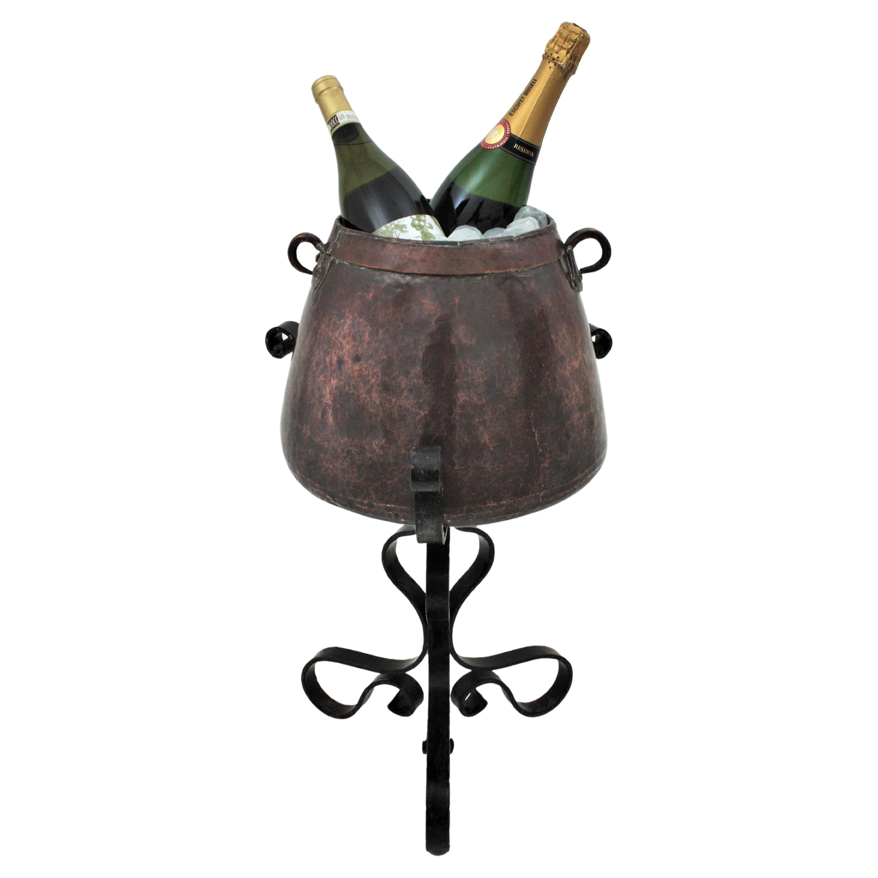 One of a kind hand forged copper and iron cauldron wine cooler on stand, Spain, 1920s-1930s.
This tripod stand champagne serving set is all made by hand. The handwrought iron stand has a tripod base with loop shaped feet and supports a large