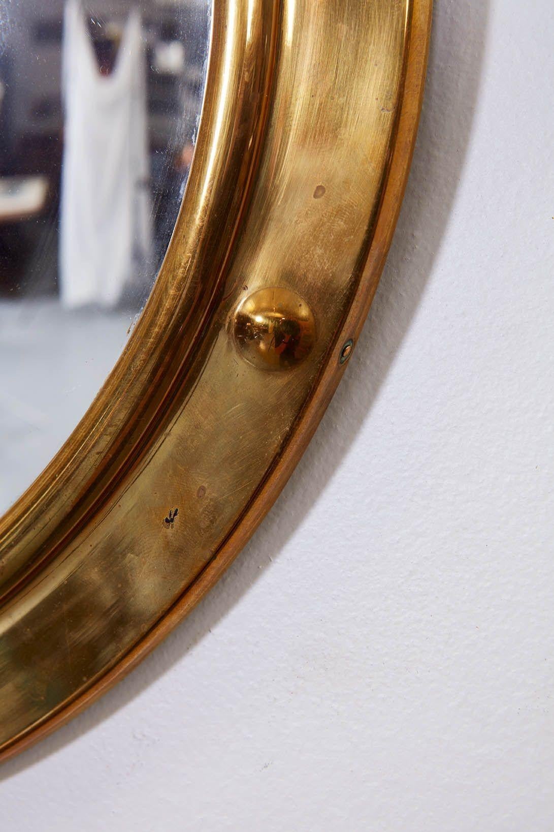 A round mirror with convex glass surrounded by a molded copper frame featuring eight raised roundels. Ideal for a powder room or a room with a nautical theme.