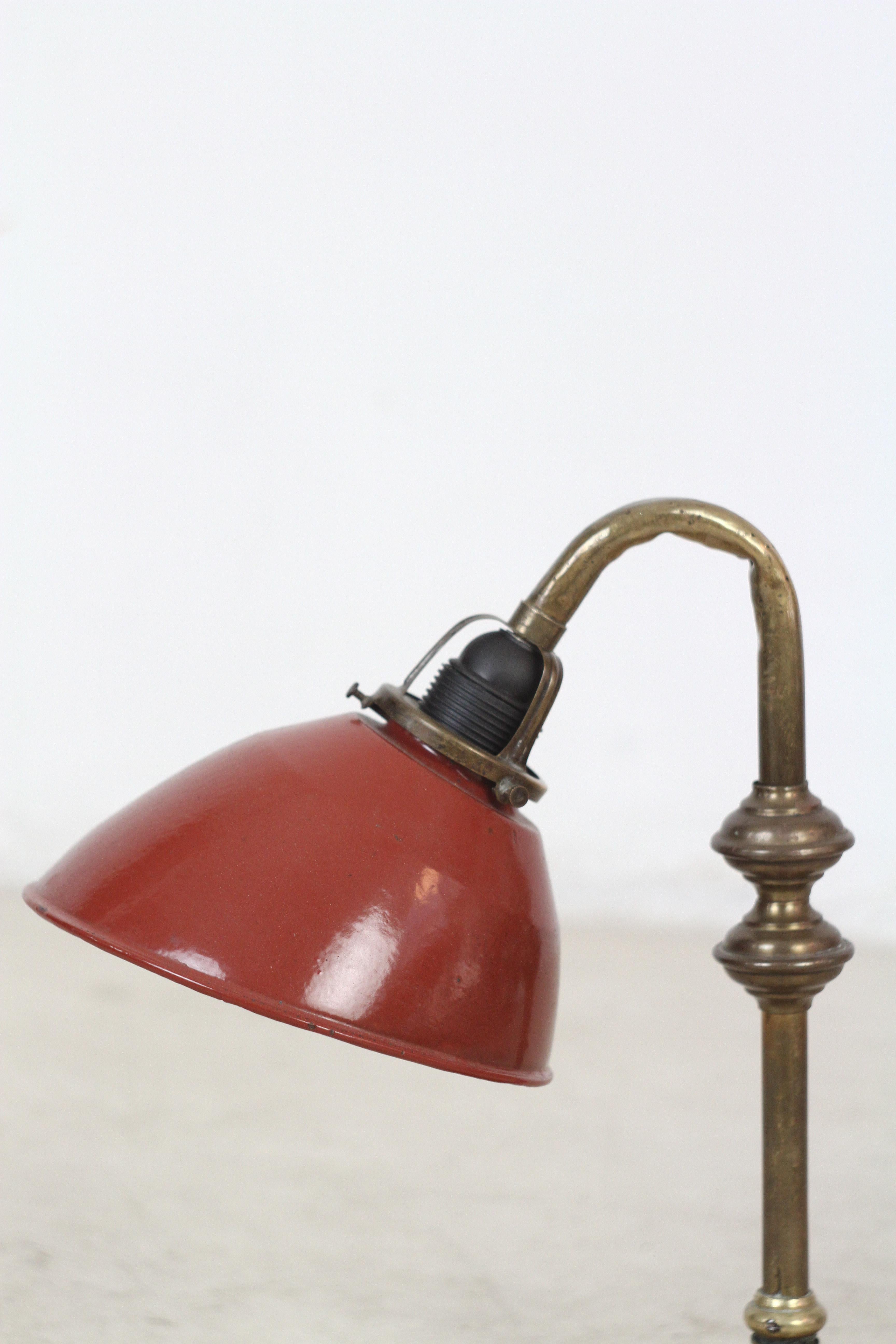 Ornate and beautifully made 1920s desk lamp with frame and base of patinated copper and brass. Its mounted with the original burgundy red enameled iron shade. The socket was changed fitting for E27 large lightbulb.