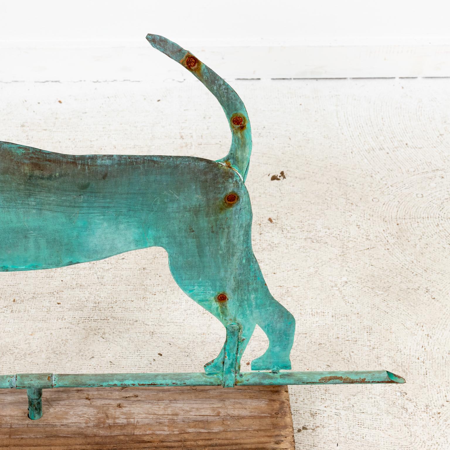 Circa 20th century Folk Art style Copper hound dog weathervane with verdigris patina, mounted on rustic pinewood stand base. Made in the United States. Please note of wear consistent with age including some rusted, oxidized rivets due to exposure to