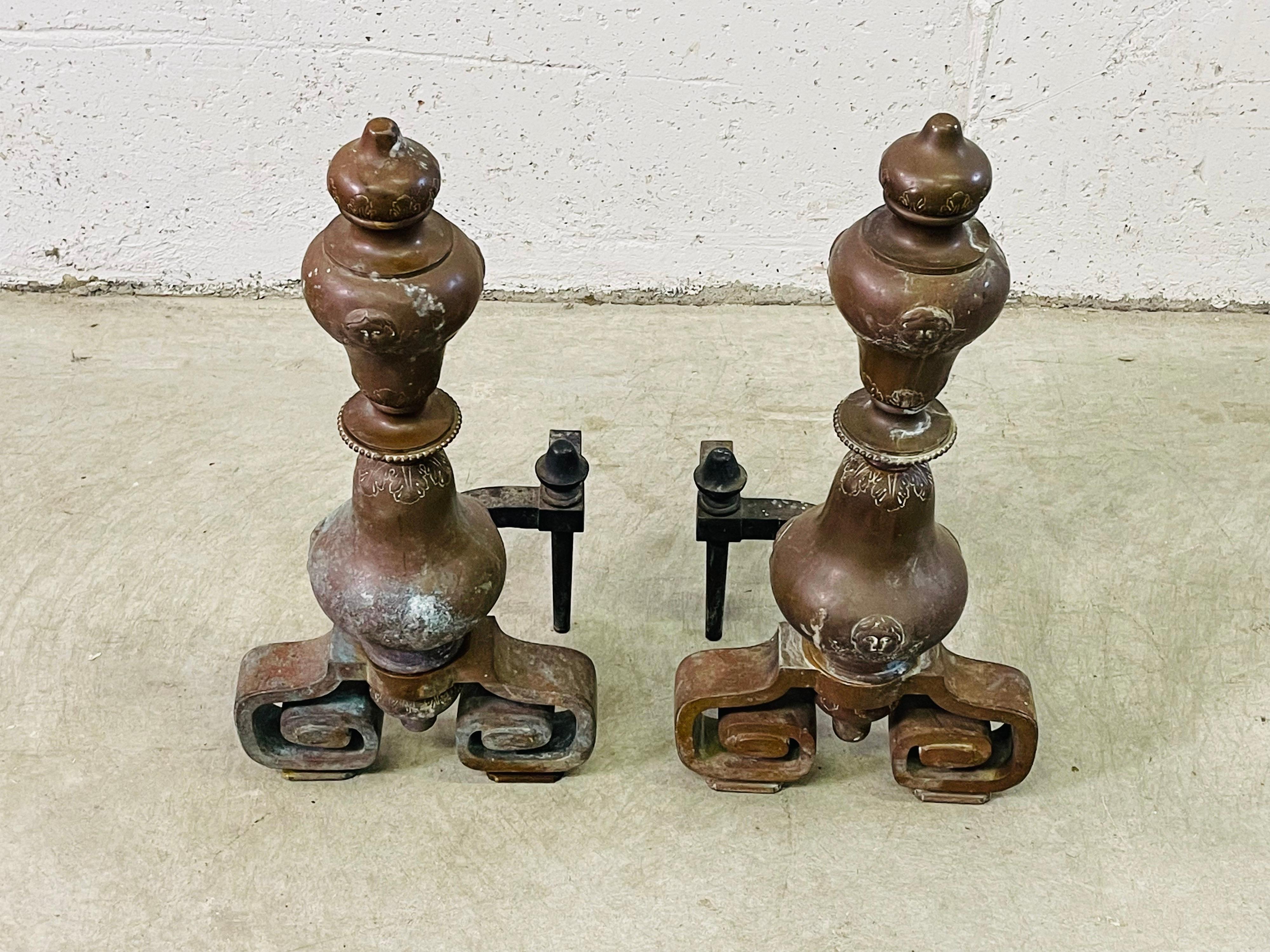 Vintage pair of copper andirons with an Asian styled iron base. The andirons have an incised design that includes what looks like childrens faces. The andirons need to be restored because of the tarnish to the copper. But they are solid and sturdy.