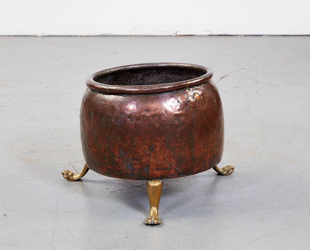 A copper log bin of rounded form having a rolled rim and flat base supported on three lion paw legs, and featuring a nicely patinated finish.