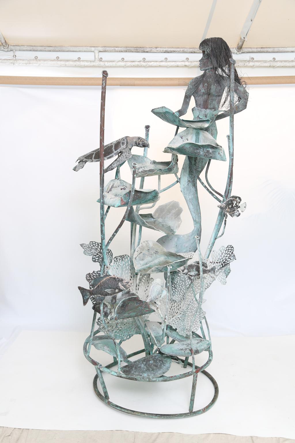 Whimsical fountain sculpture, of copper, by metal artist Glen Mayo; its mermaid focal point holding a leaf which cascades water down the fountain, among turtles, angel fish, other sea life, and coral. 

Stock ID: D2499.