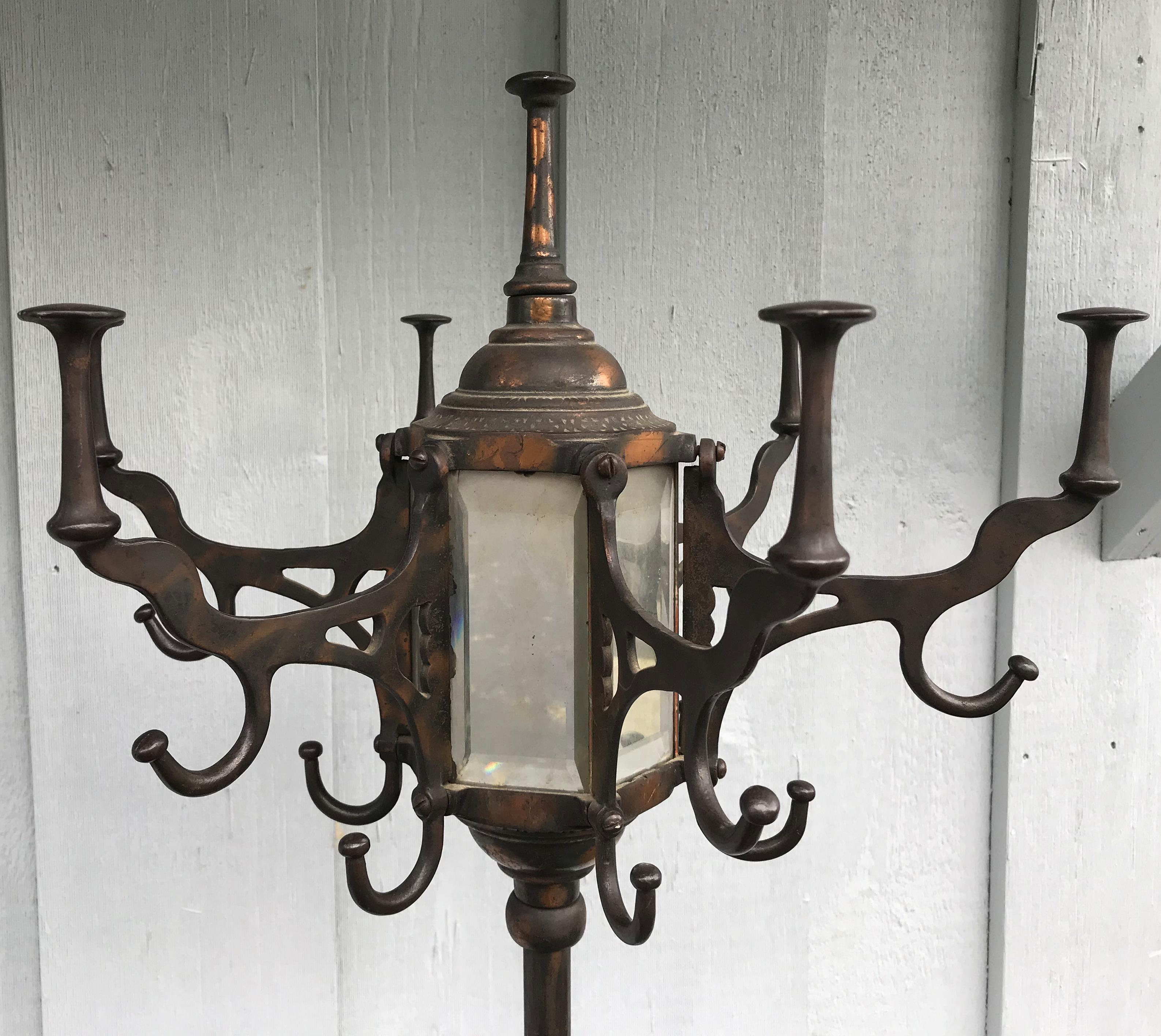 A wonderful copper patinated metal coat tree or hat rack with beveled mirror panels, multiple hooks for coats and hats, an umbrella and cane holder near the star decorated base with catch, supported by four metal legs with small pad feet. Dates to
