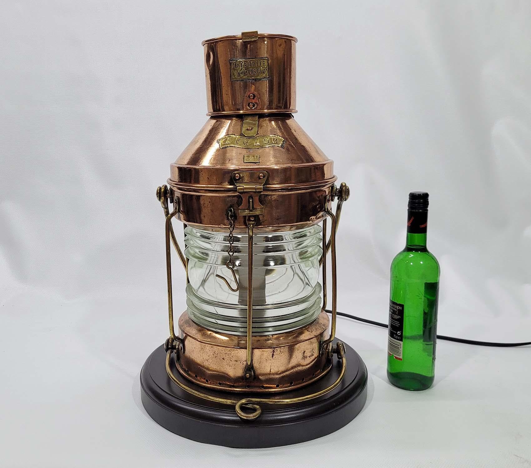 Copper ships anchor lantern by English Maker meteorite. With brass makers badge bearing serial number 90607. Clear glass Fresnel lens. Brass hoisting handle. Hinged top. Wired with electric circuit. Mounted to a thick wood base. This lantern has
