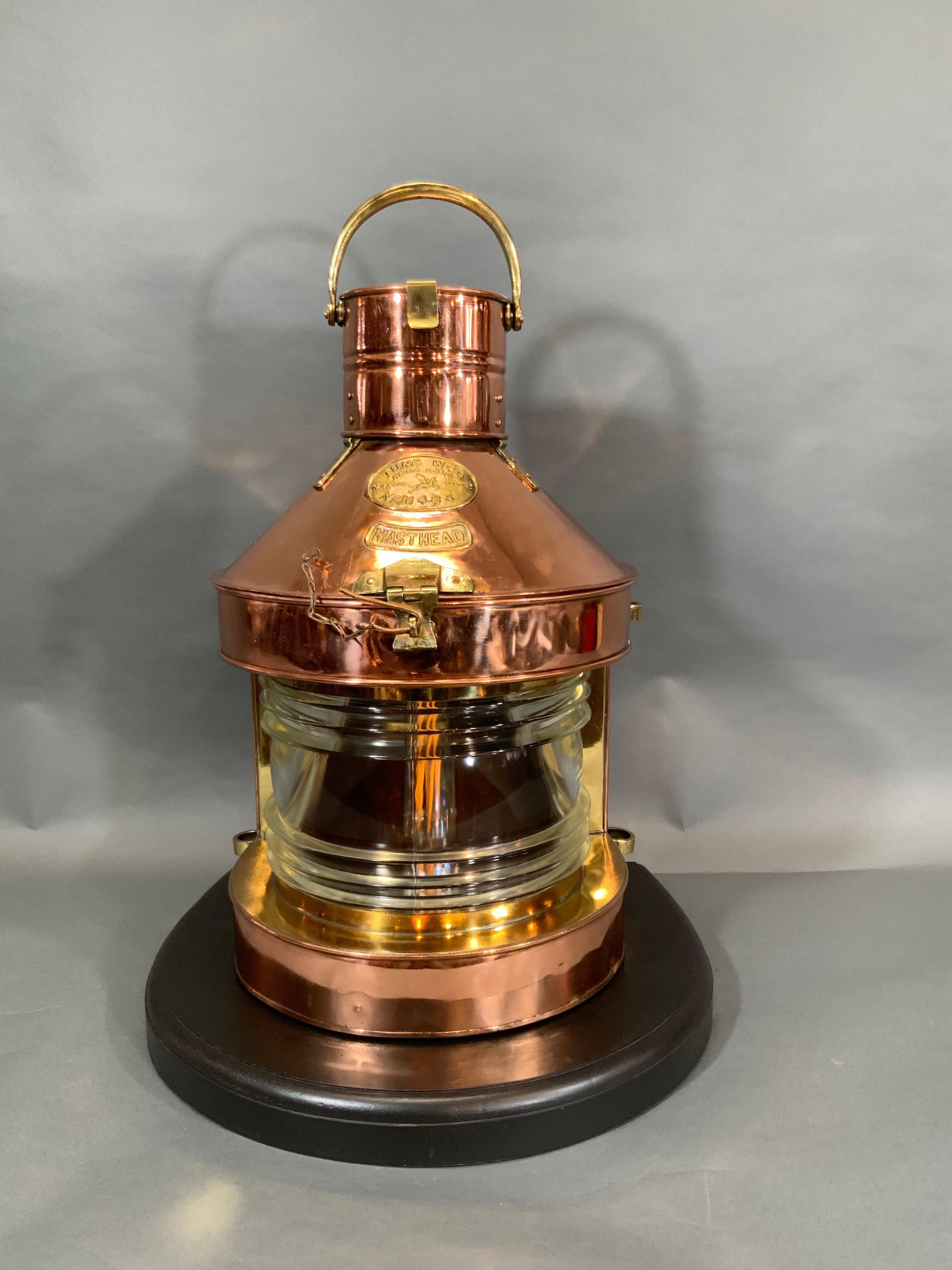 Tung Woo ship's masthead lantern that has been meticulously polished and lacquered. With hinged top, brass badges, Fresnel glass lens, hoisting handle, bracket rings, etc.. Also mounted to a thick mahogany base. First class presentation of a great